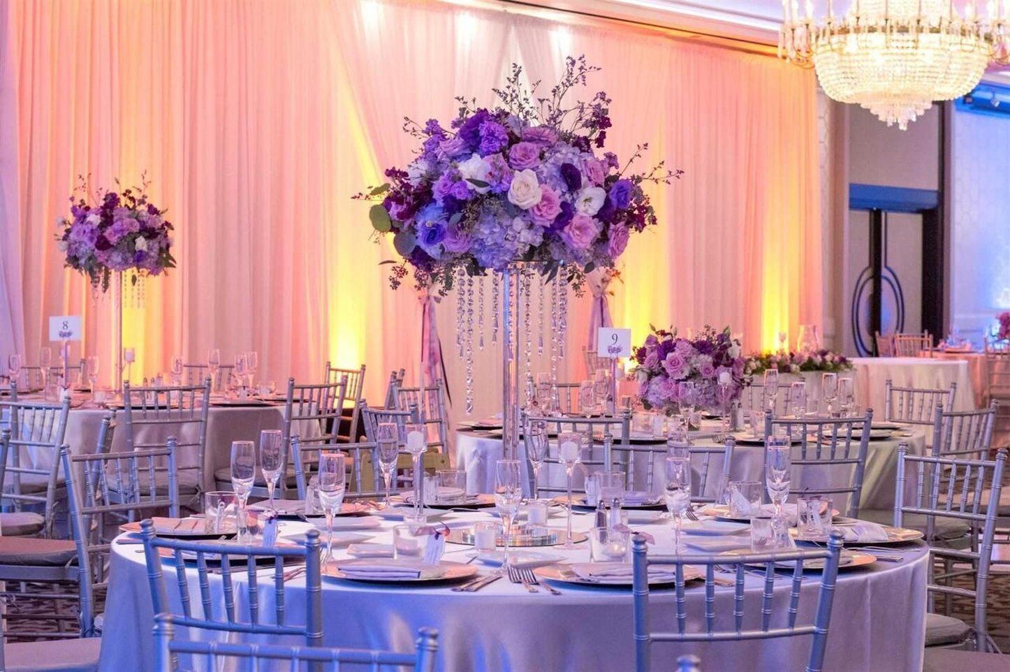 Un salón de banquetes con mesas redondas, sillas y centros de mesa florales.
