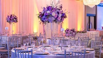 Un salón de banquetes con mesas redondas, sillas y centros de mesa florales.
