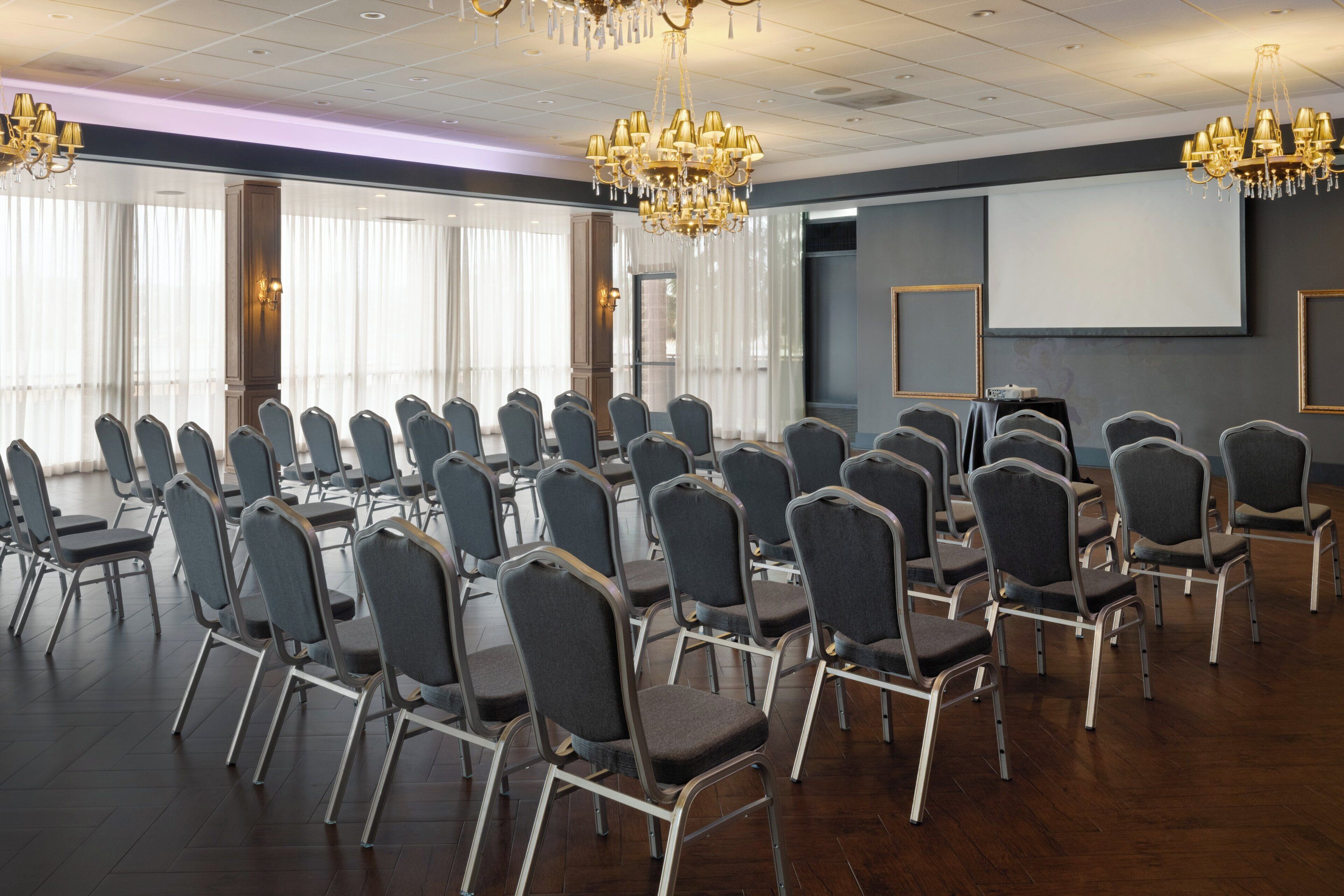 A conference room with rows of chairs, a projector screen, and chandeliers.