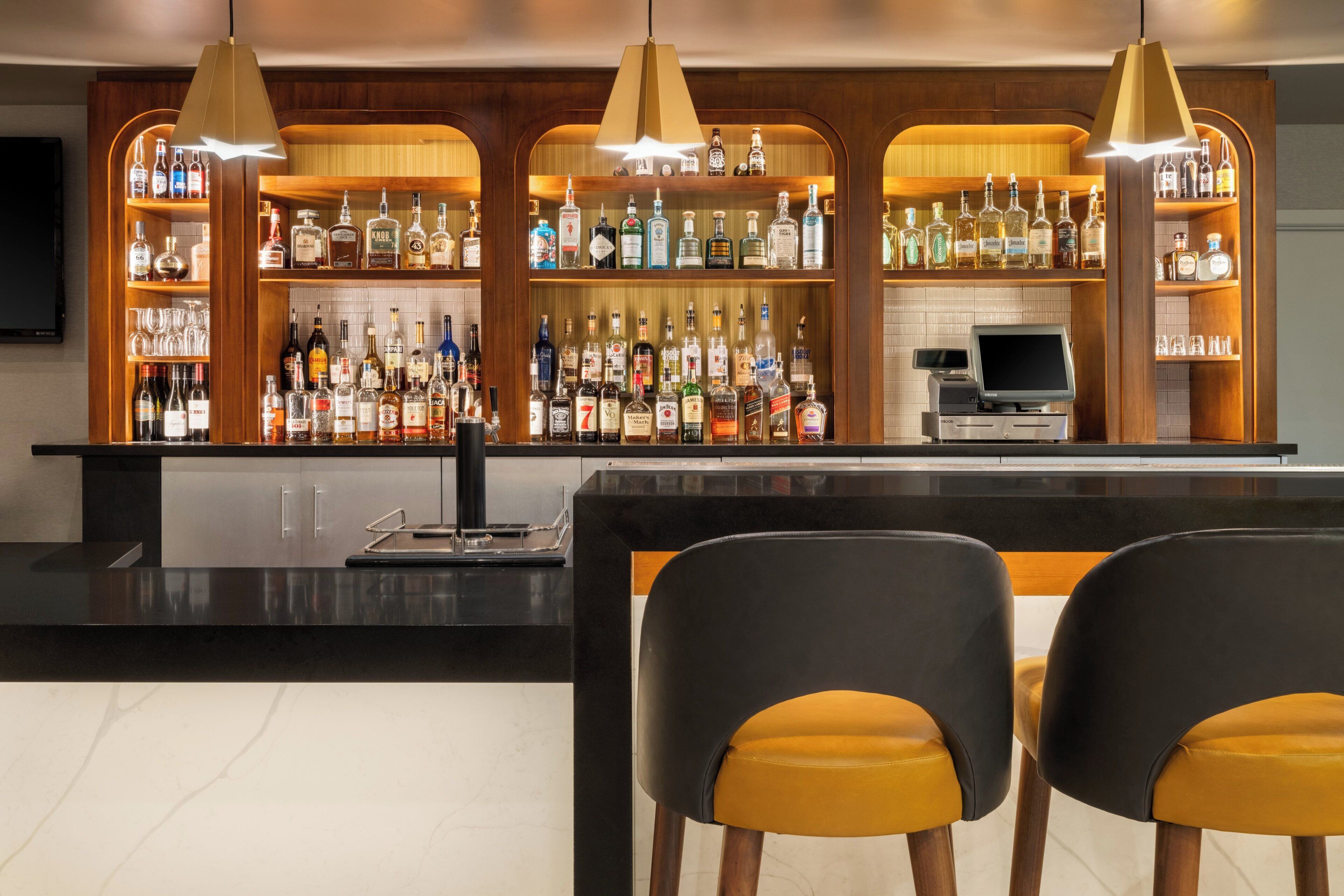 Un espace bar comprenant un comptoir, plusieurs étagères remplies de bouteilles d’alcool et deux tabourets de bar.