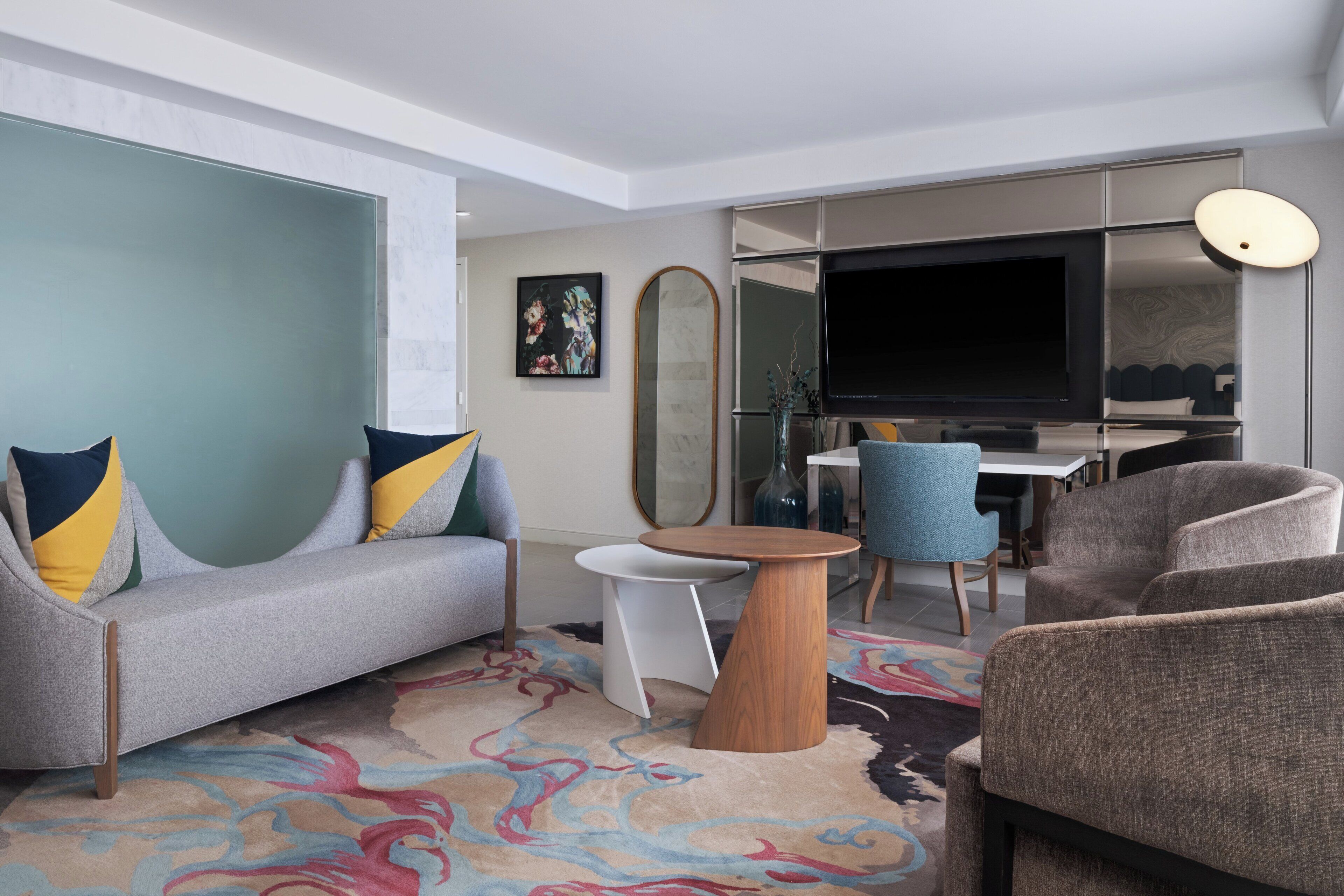 Una sala de estar moderna con un sofá, sillones, una mesita redonda, un televisor de pantalla plana y un espejo grande.