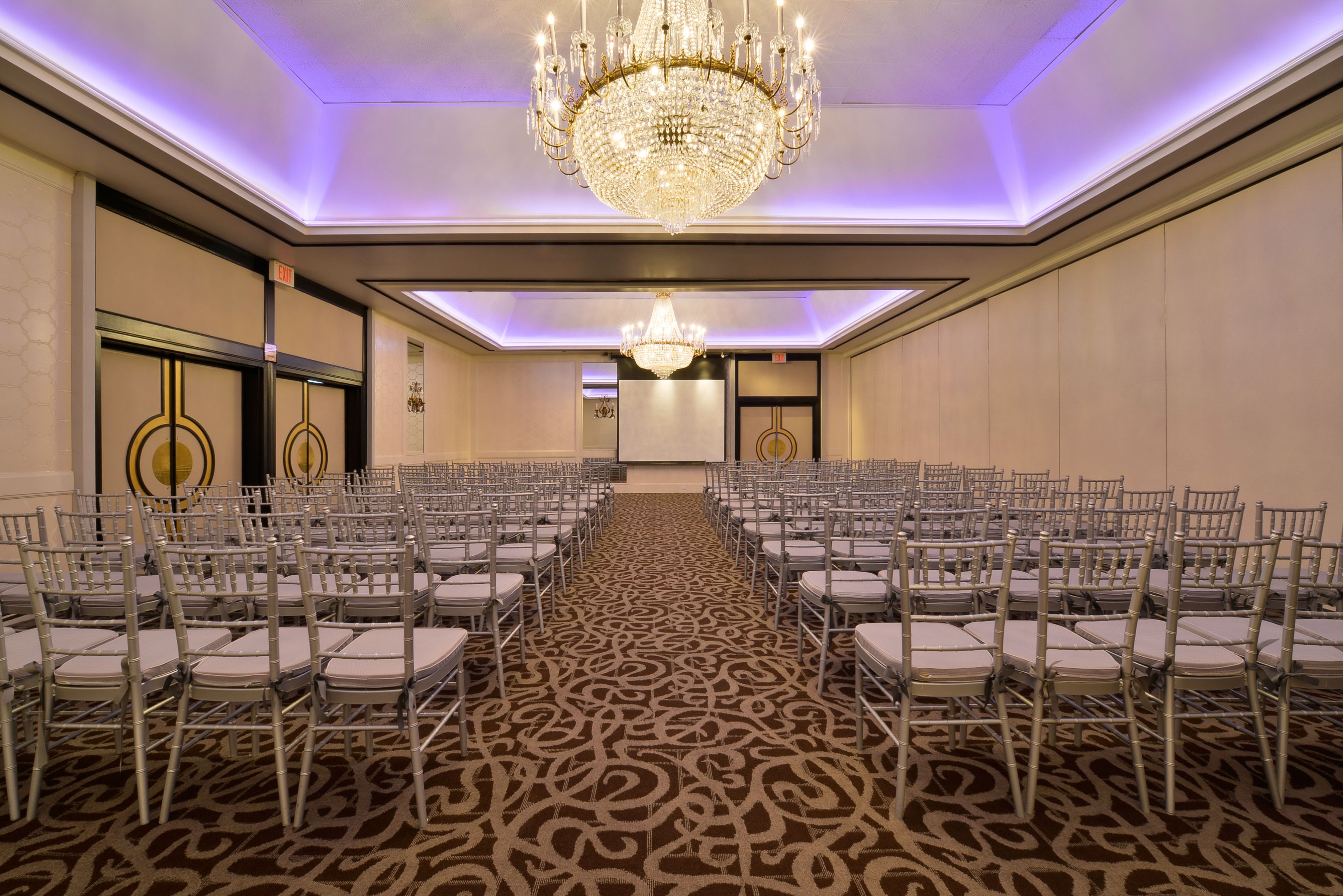 A conference room with rows of chairs, a large chandelier, and a patterned carpet.