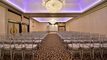 A conference room with rows of chairs, a large chandelier, and a patterned carpet.