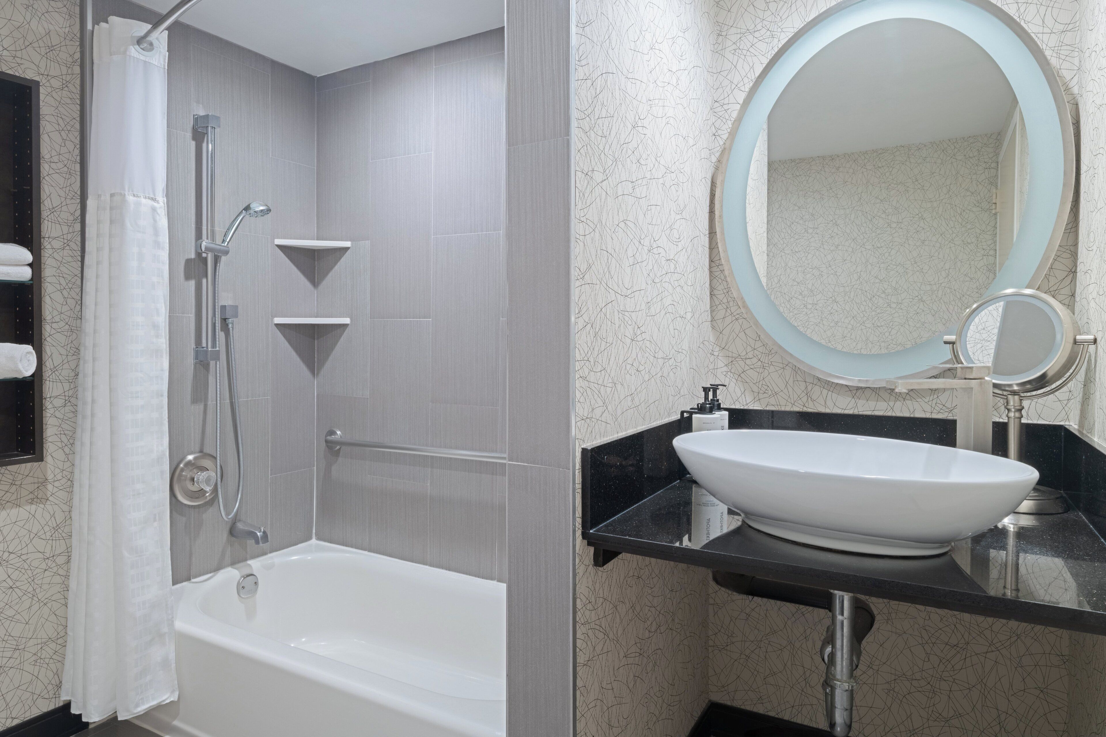 A modern bathroom with a bathtub, shower, and a vanity with a sink and mirror.