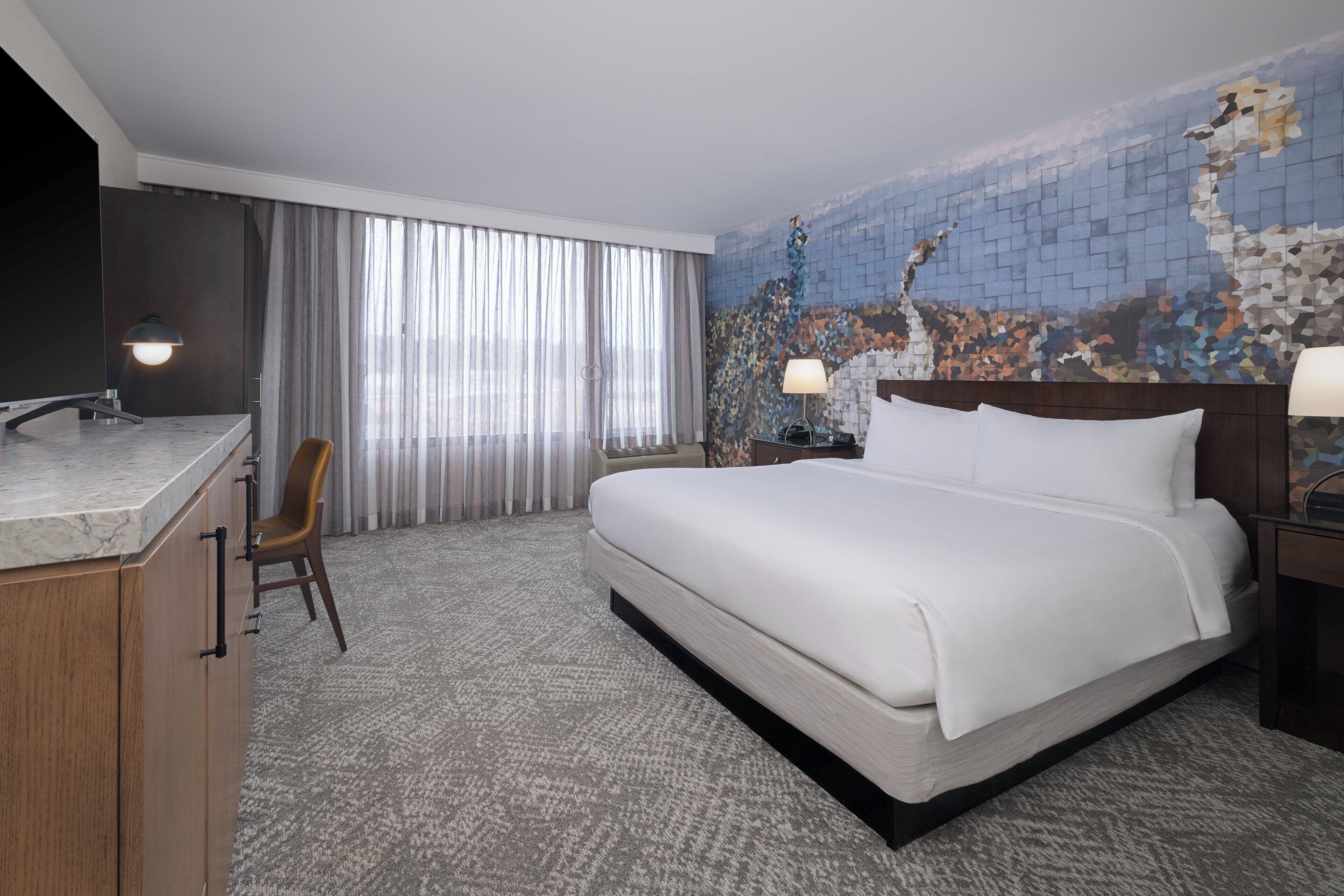 Een hotelkamer met een bed, een bureau, een stoel, een televisie en een groot raam met gordijnen.