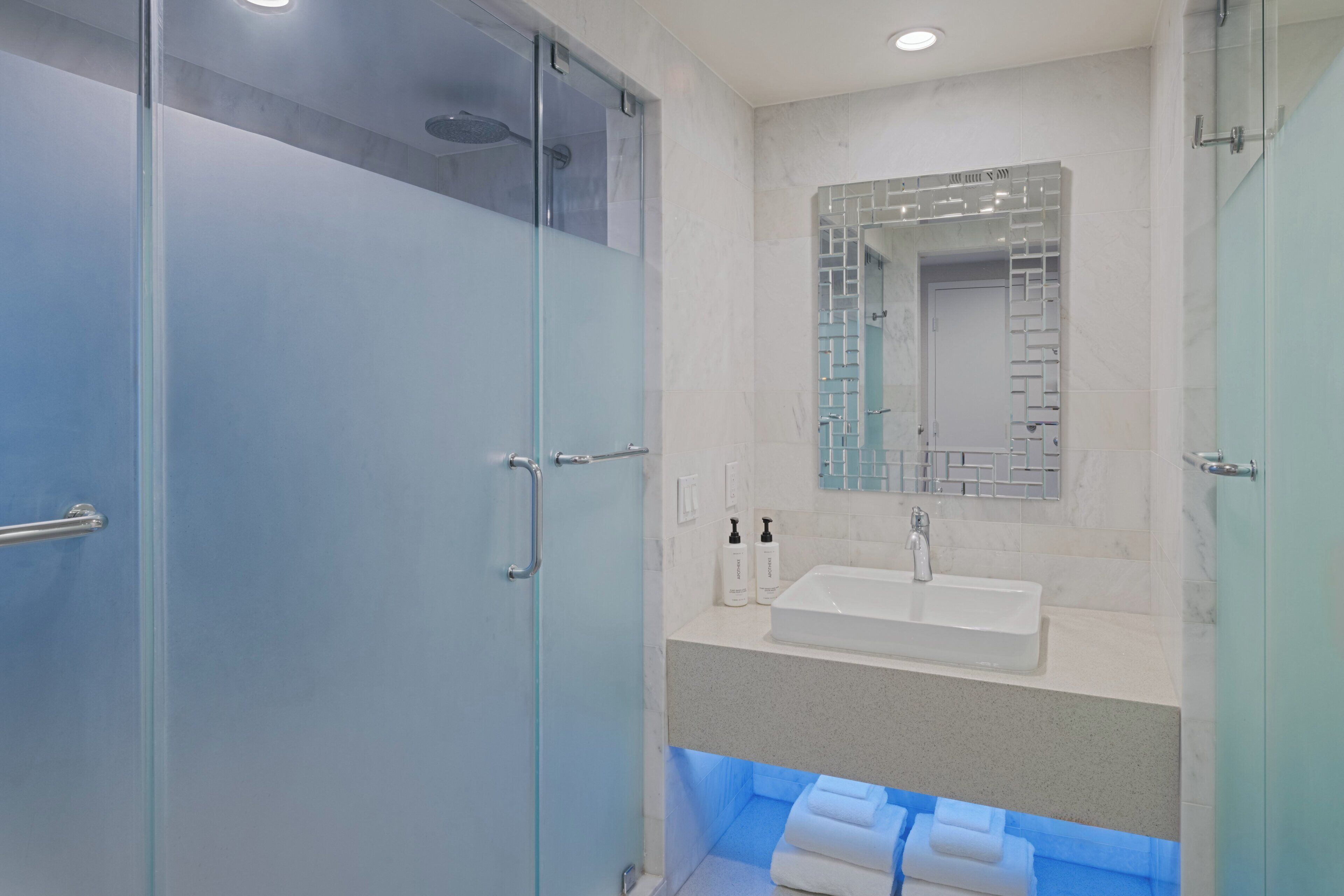 A modern bathroom with a glass shower enclosure, a sink, and a mirror with a decorative frame.