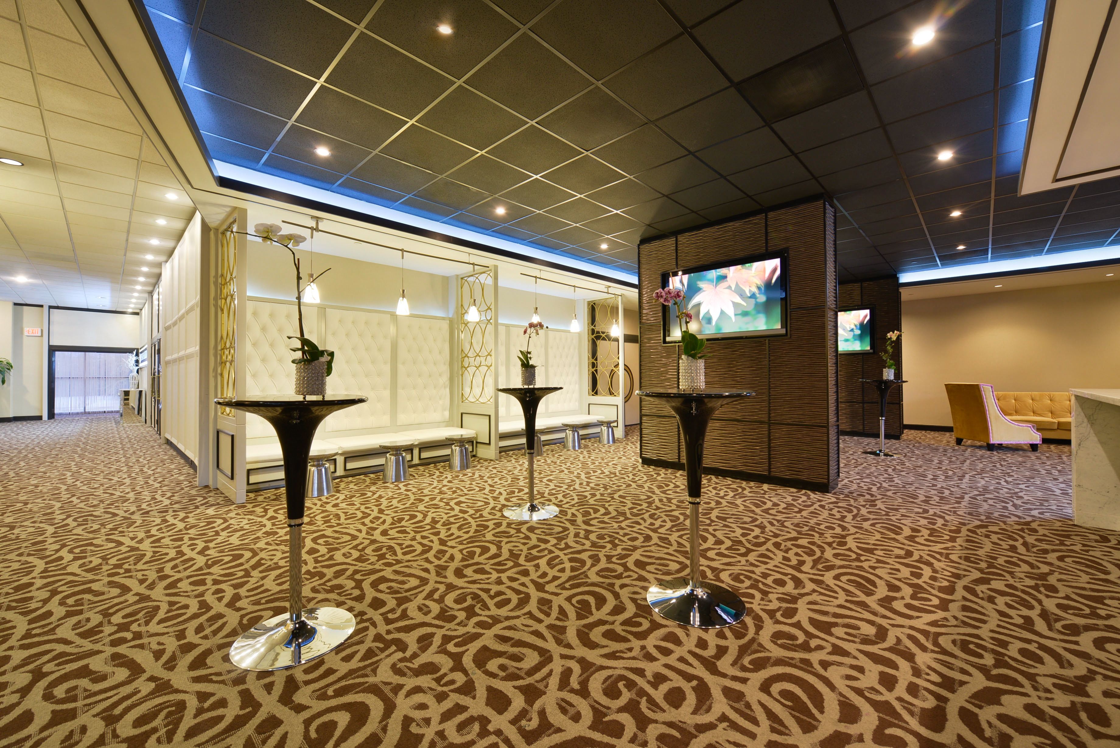A lobby with patterned carpet, modern furniture, and a television screen.