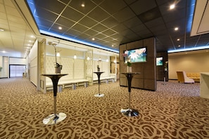 A lobby with patterned carpet, modern furniture, and a television screen.