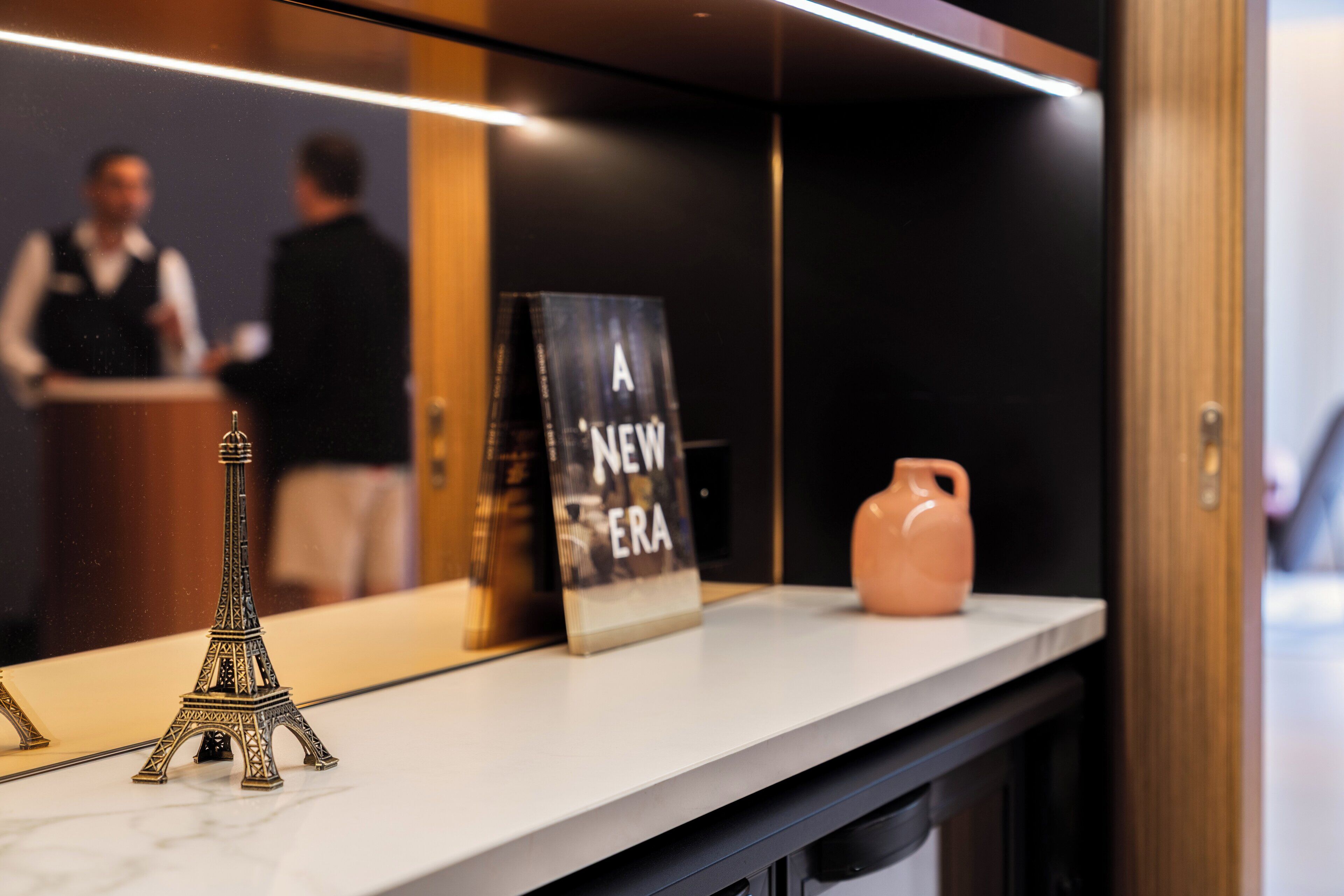 A reception desk with a small Eiffel Tower model, a sign reading "A NEW ERA," and a pink vase.