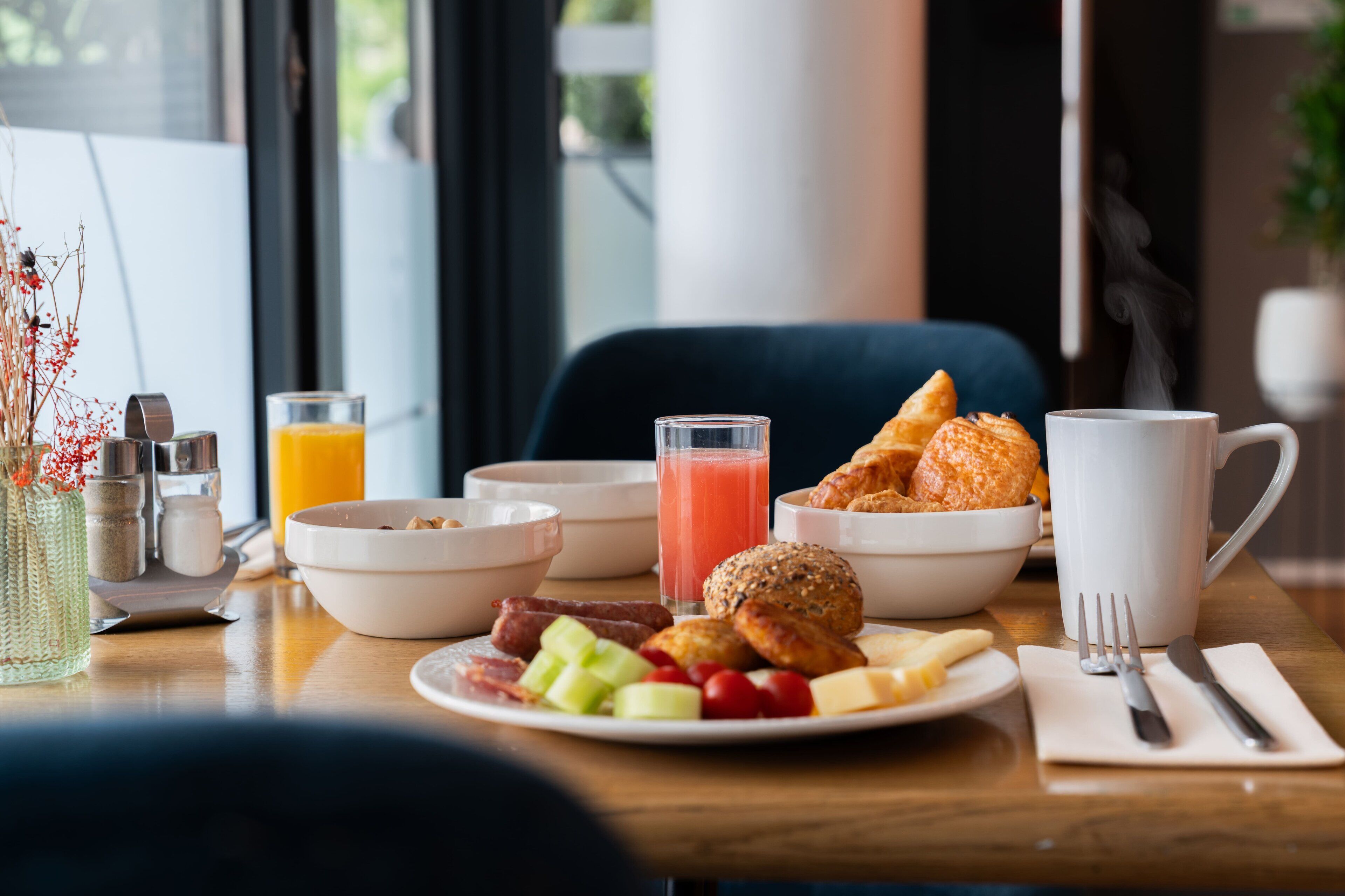 A breakfast table with various food items, a glass of orange juice, and a white mug.