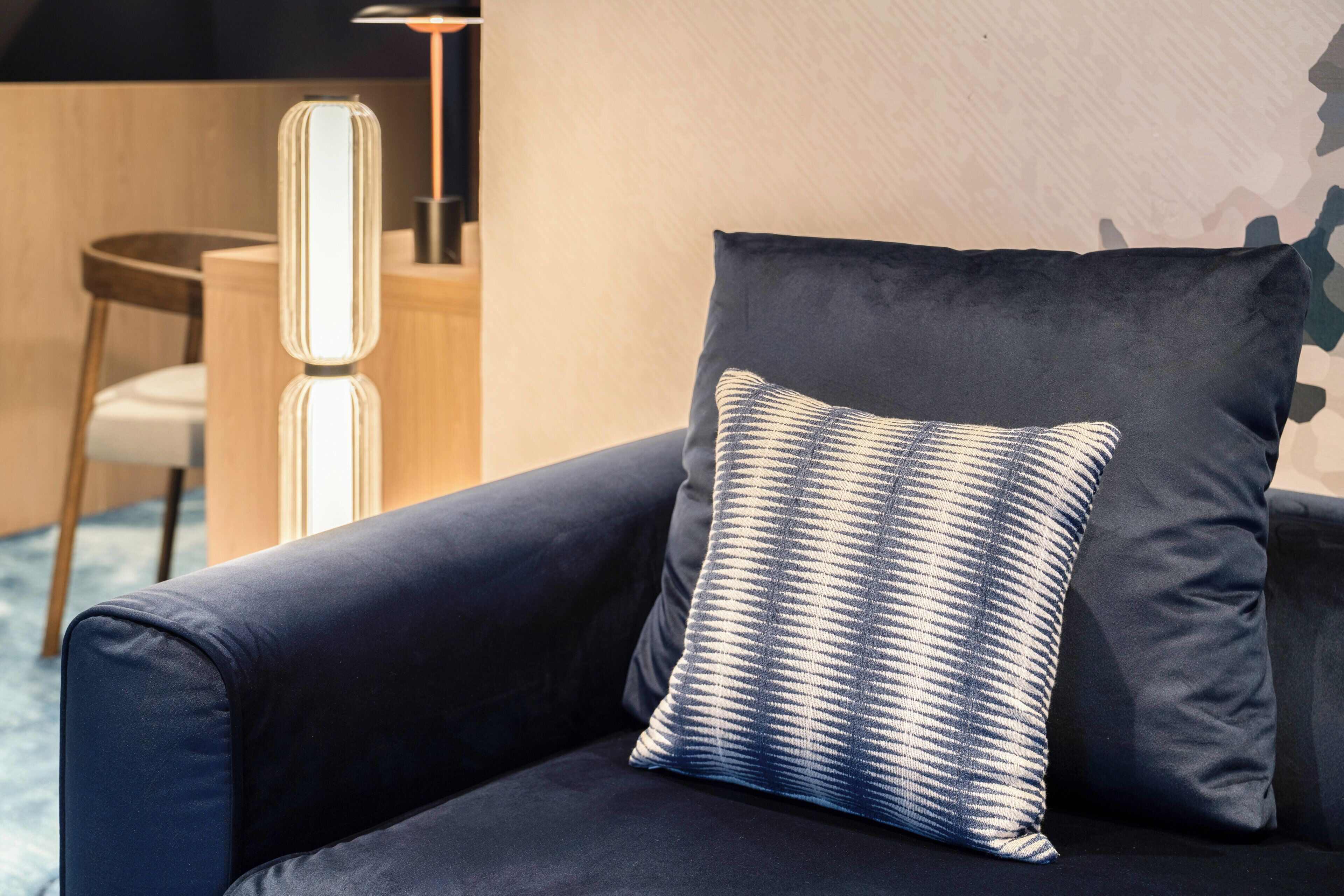 En soffa i mörk färg med en mönstrad kudde, en modern lampa och ett litet bord i trä.