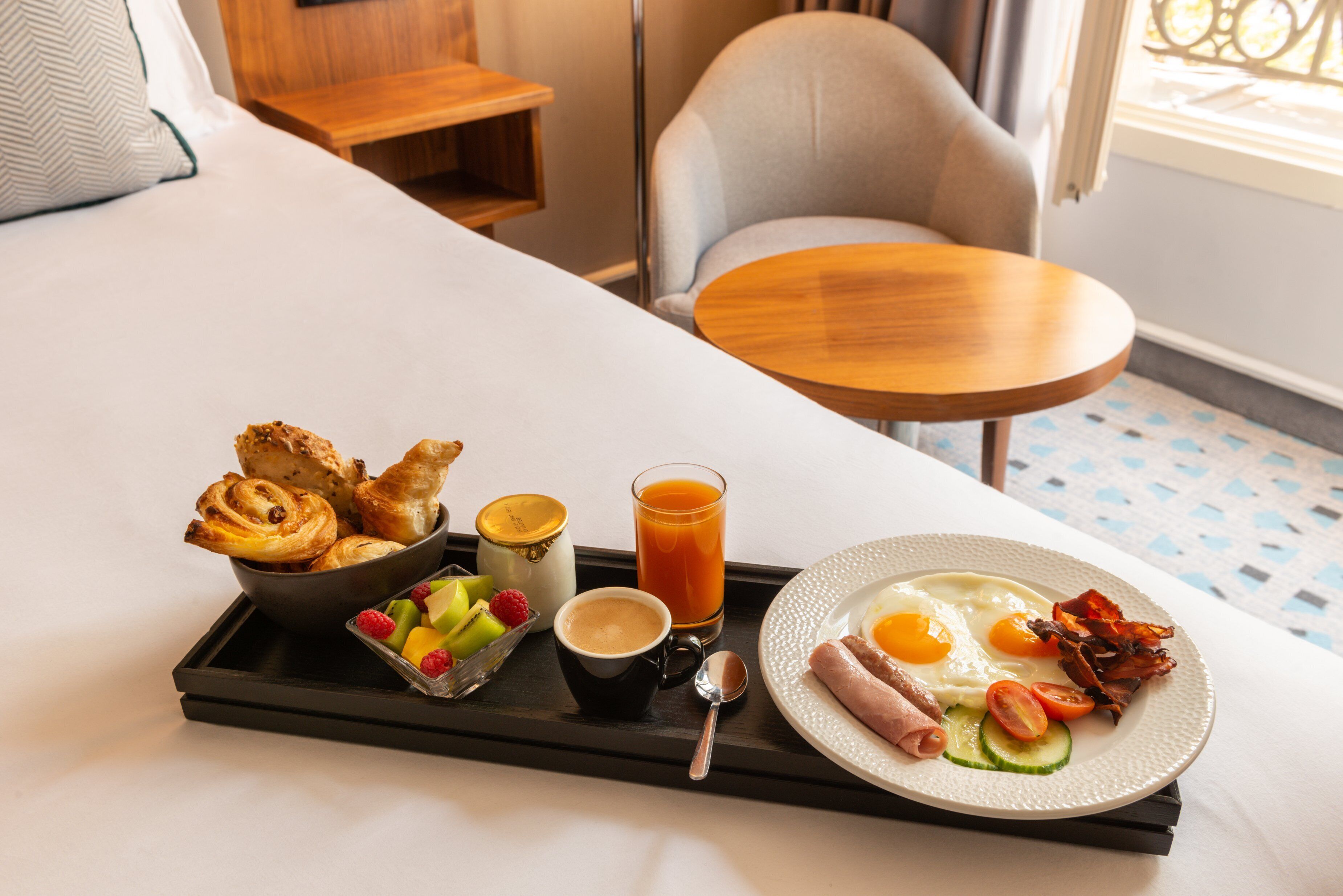 A breakfast tray with croissants, fruit, coffee, orange juice, and a plate with eggs, bacon, and vegetables.