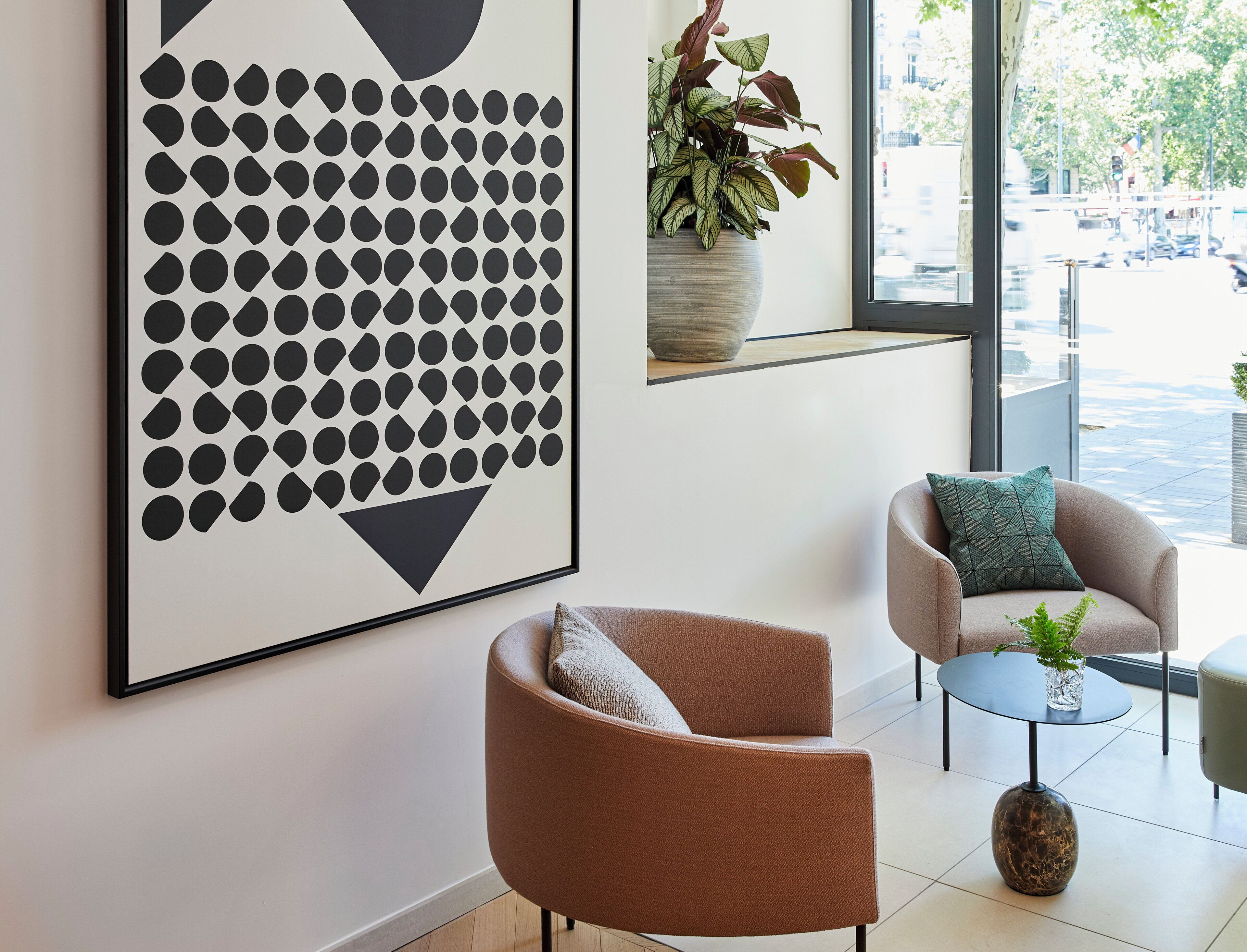 A modern interior with a large abstract artwork, a seating area with two chairs, a small table, and a potted plant.