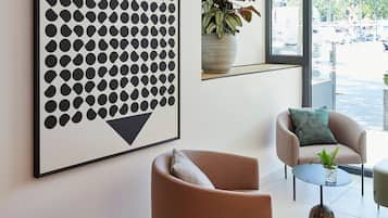 A modern interior with a large abstract artwork, a seating area with two chairs, a small table, and a potted plant.