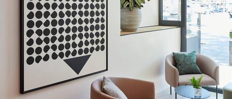 A modern interior with a large abstract artwork, a seating area with two chairs, a small table, and a potted plant.