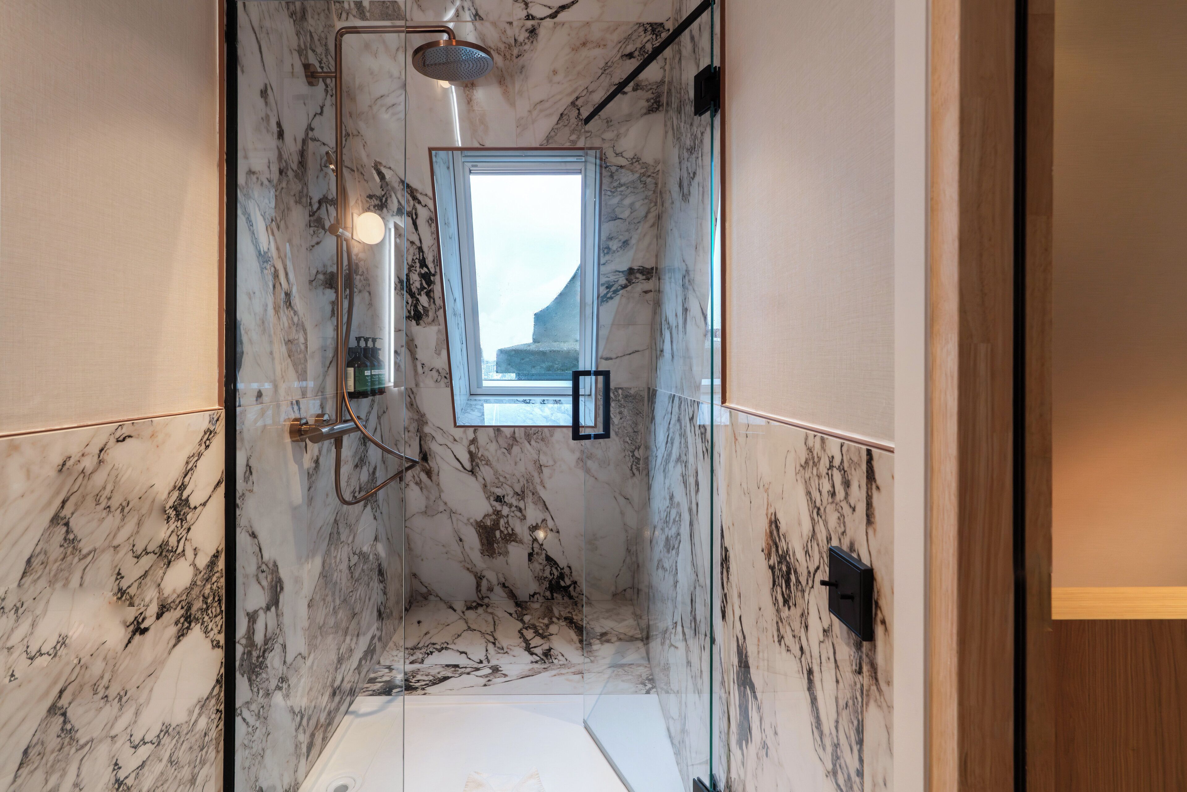 Une salle de bain aux murs recouverts de marbre, dotée d’une douche et d’une fenêtre offrant une vue.