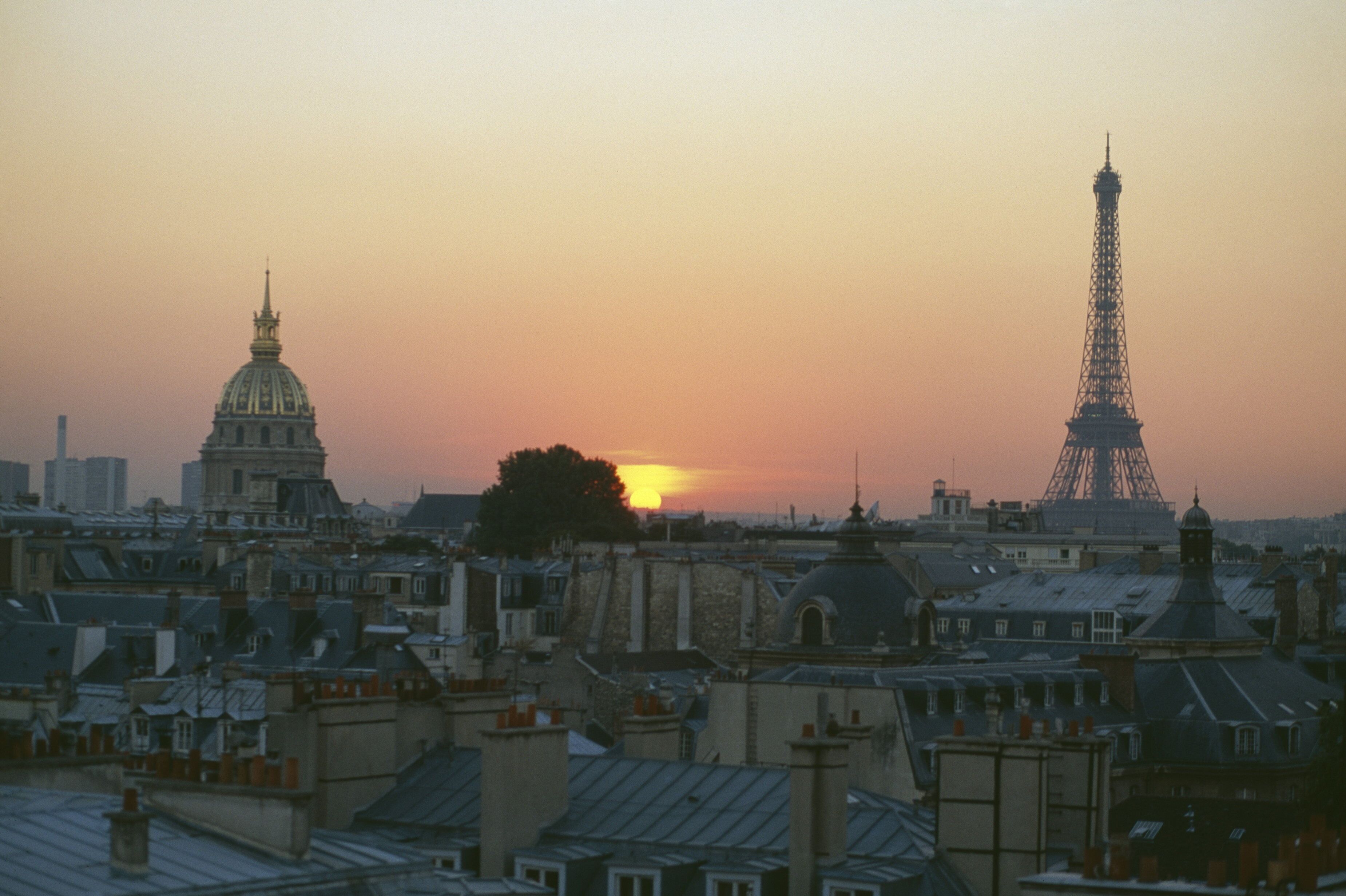 A cityscape with the Eiffel Tower and a large dome structure during sunset.