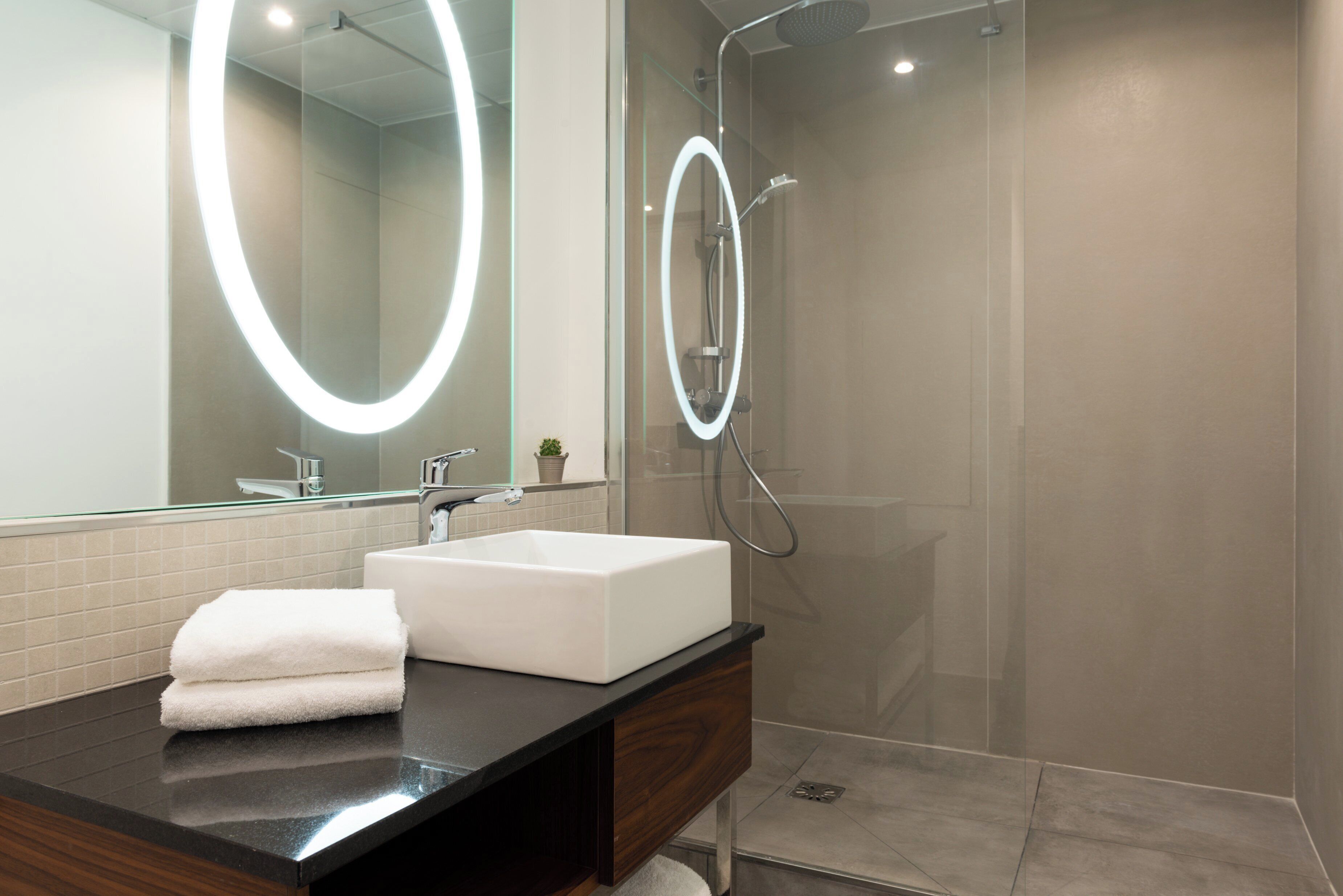 A modern bathroom with a large mirror, a white sink, and a shower.