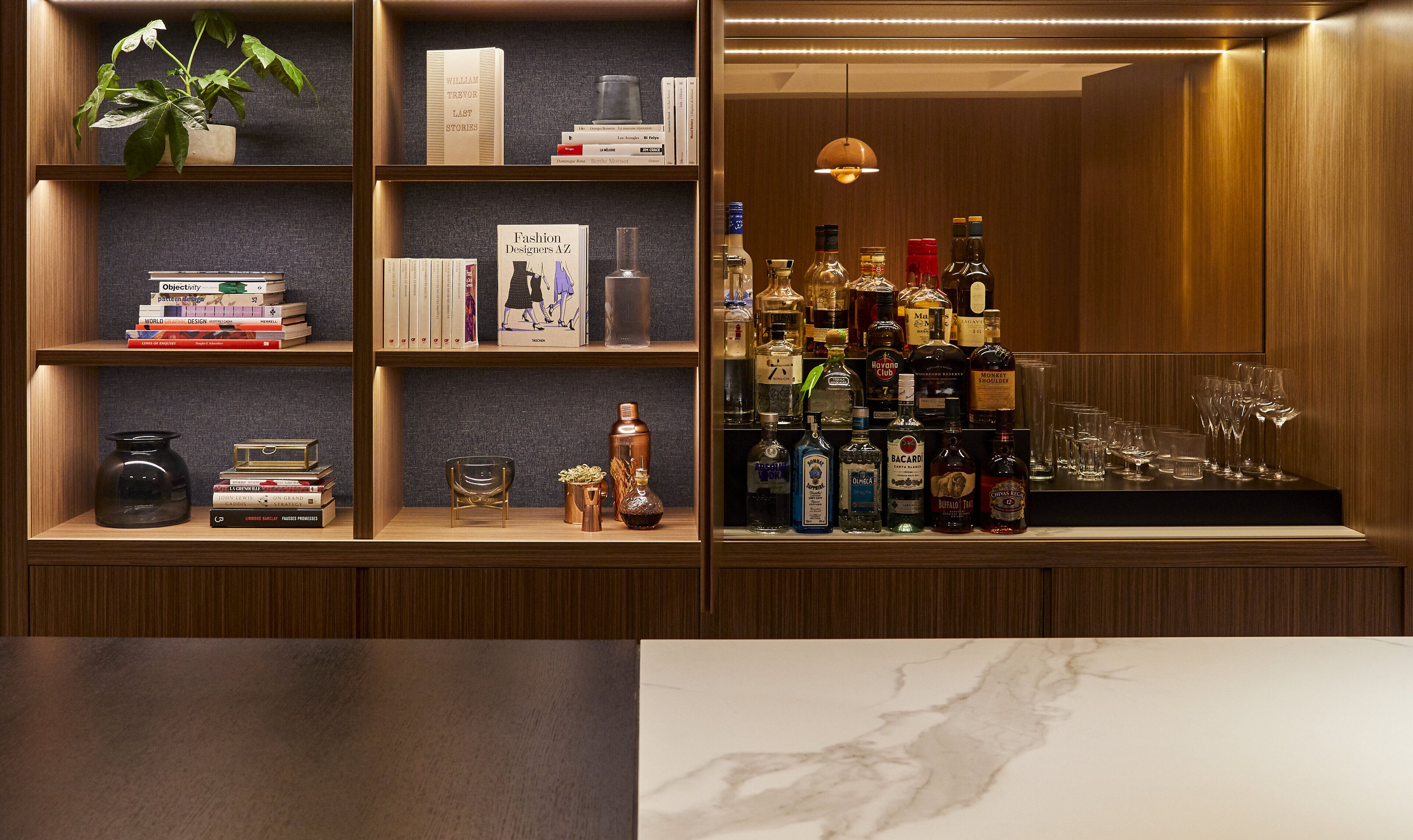 A well-organized bar area with shelves of books, bottles of liquor, and glasses.