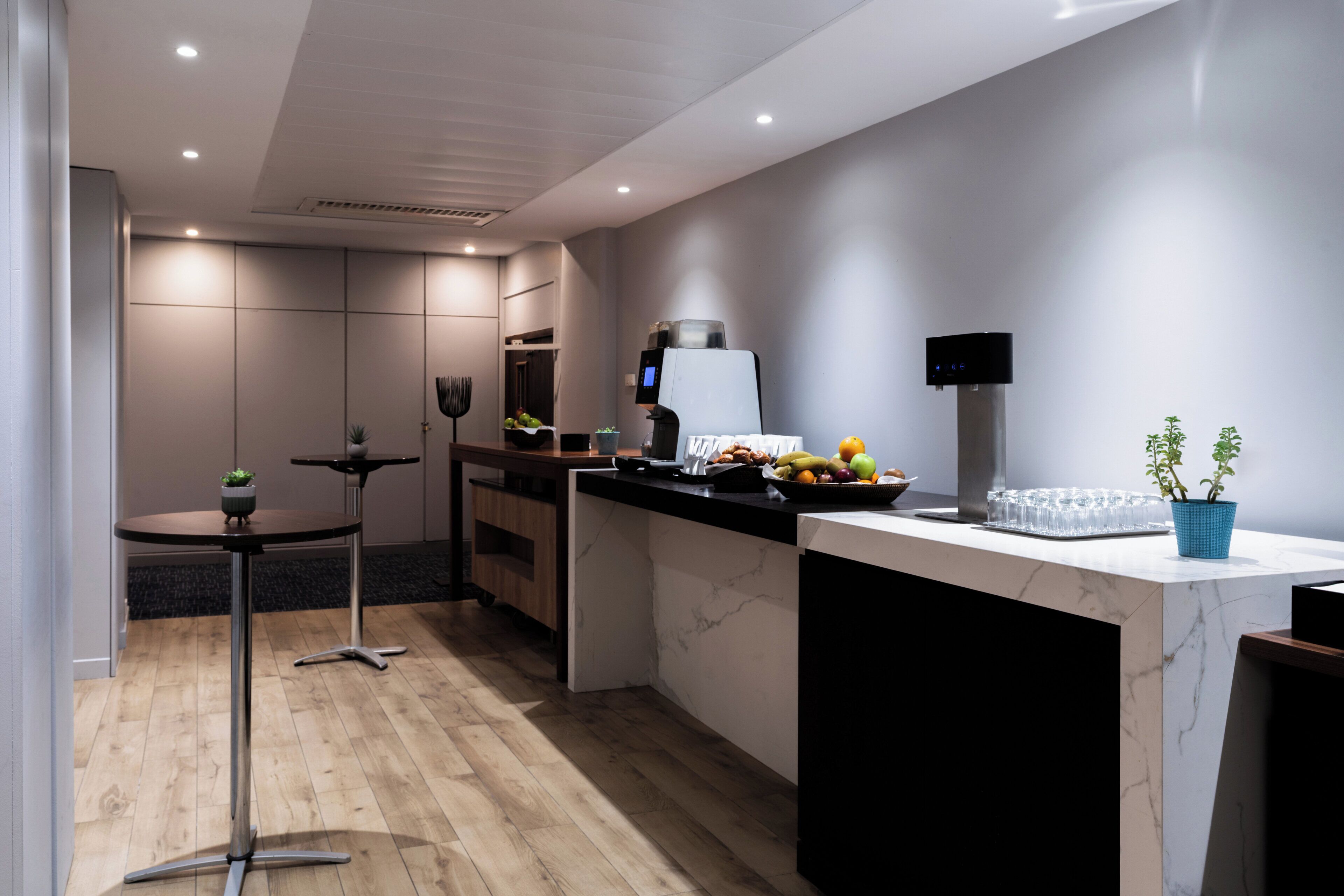 A modern kitchen with a marble countertop, a coffee machine, and a small potted plant.