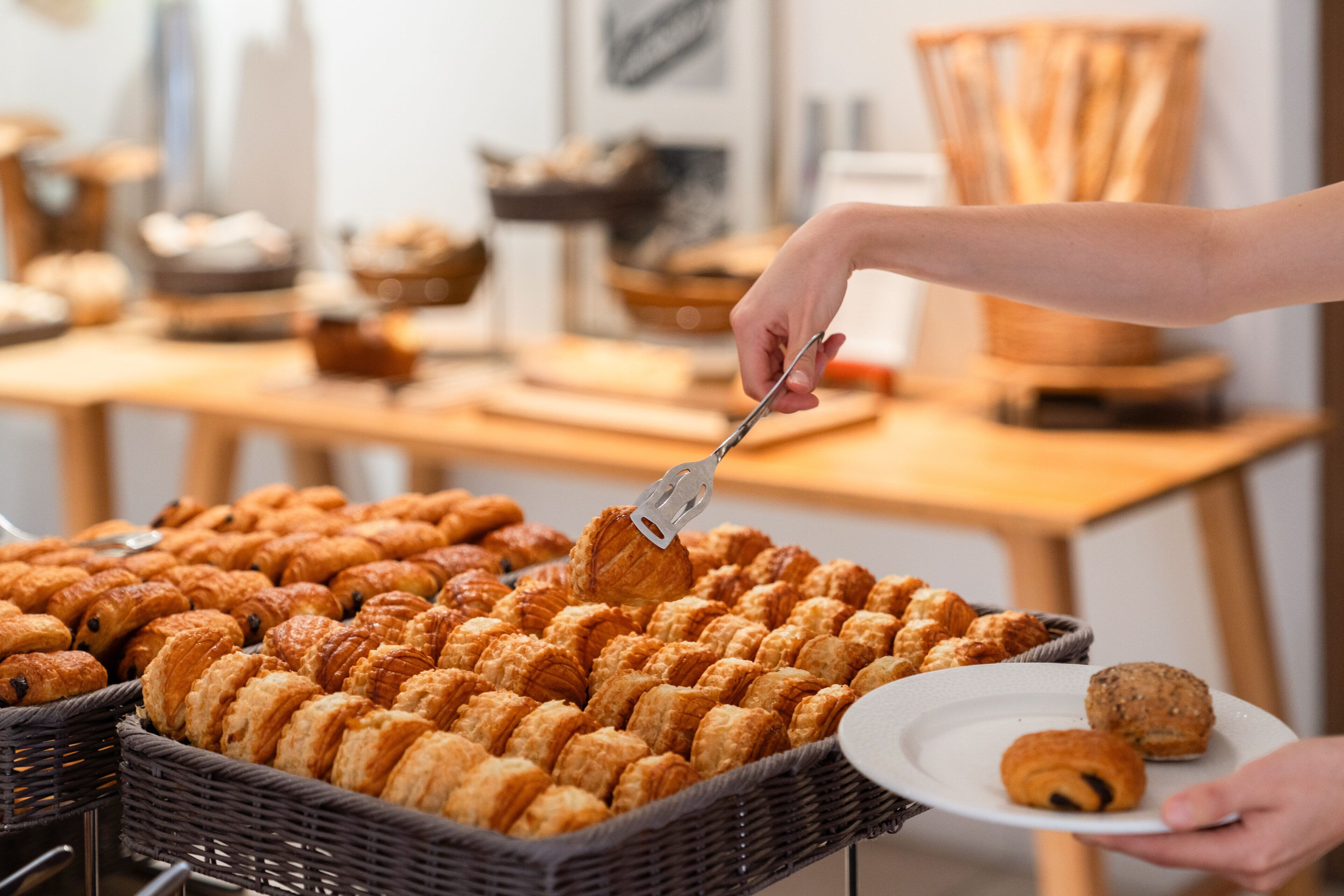 A person serving pastries from a large wicker basket.