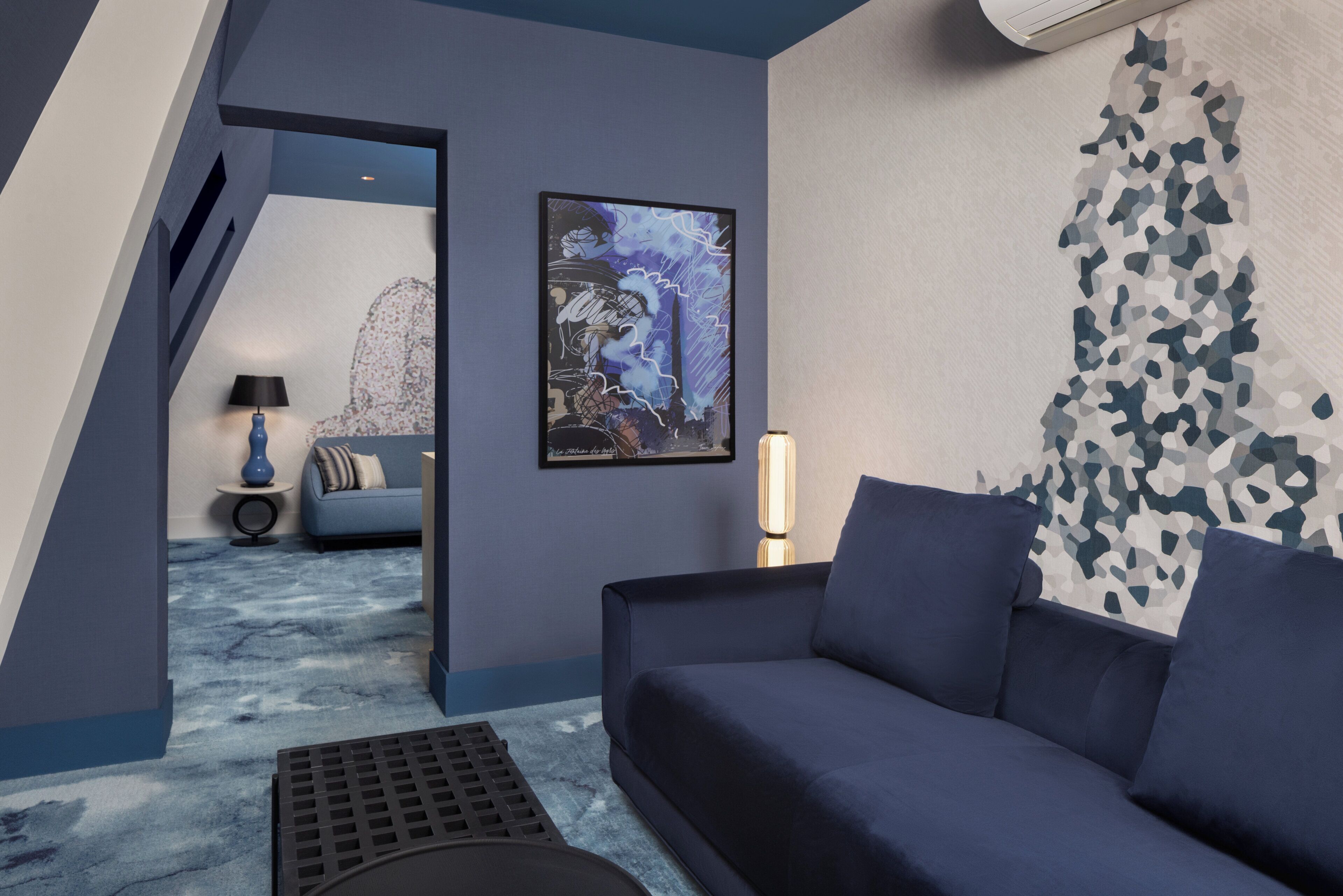 A modern living room with a dark blue sofa, a framed artwork on the wall, and a patterned wall design.