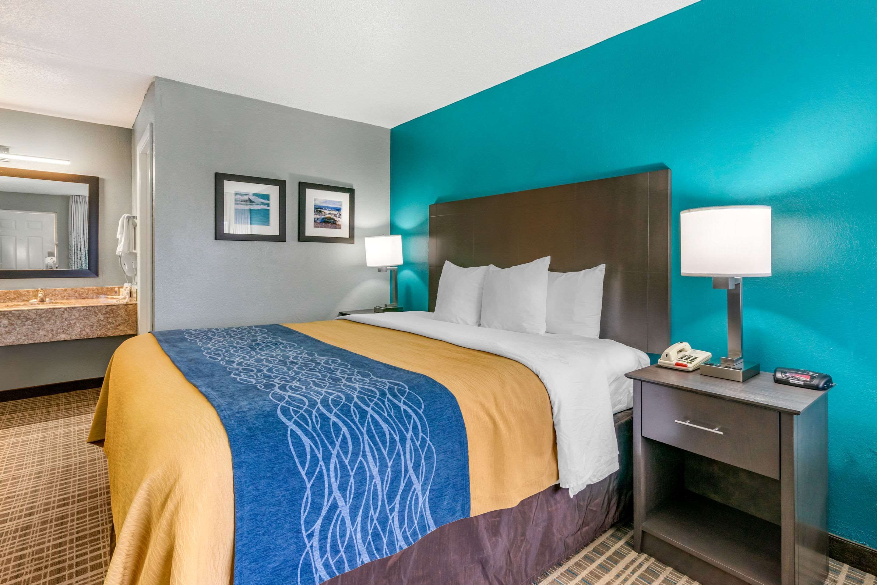 A hotel room with a bed, nightstand, and a bathroom area.