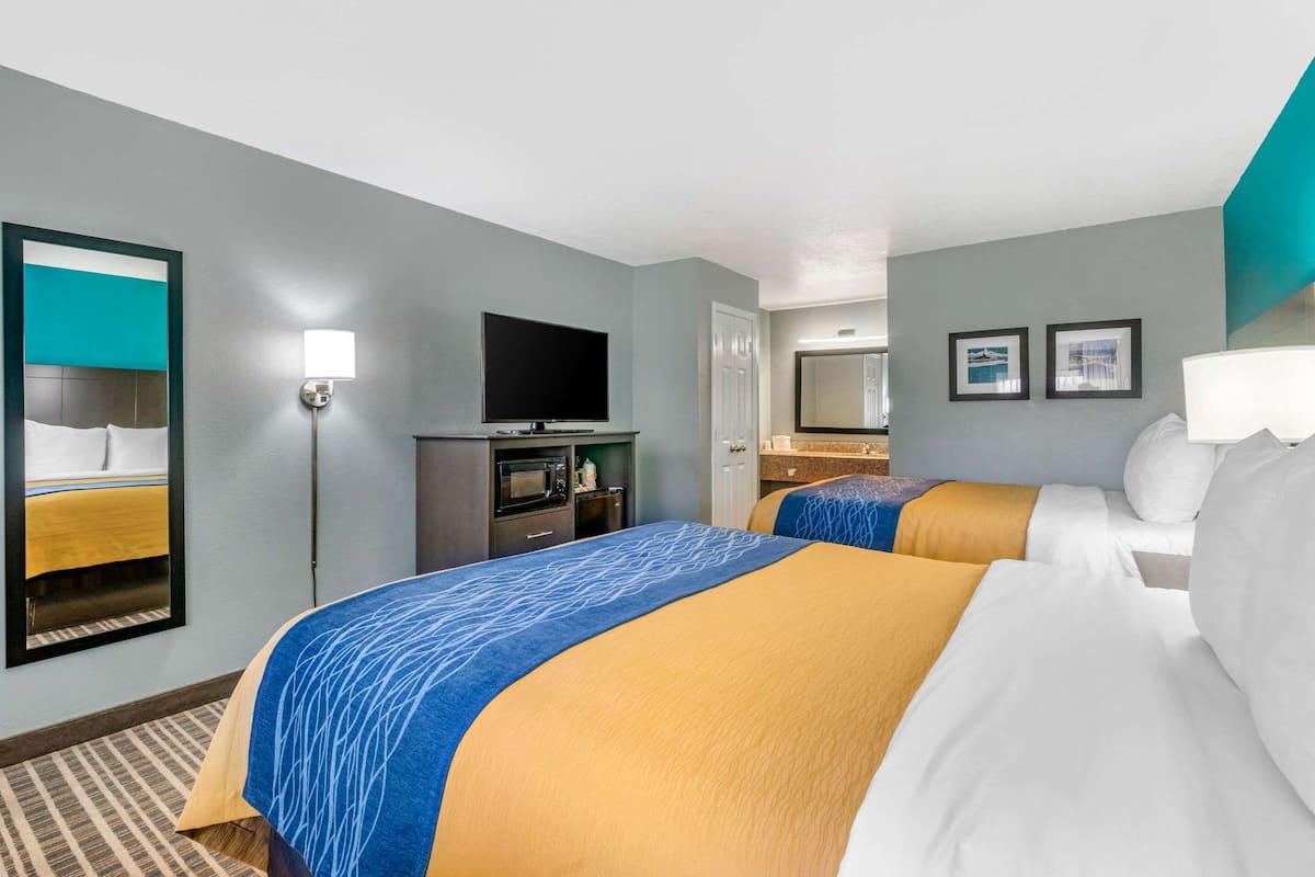 Habitación de hotel con dos camas, un televisor de pantalla plana, un escritorio con computadora, un microondas y un espejo.