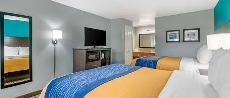 A hotel room with two beds, a flat-screen TV, a desk with a computer, a microwave, and a mirror.