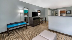 A hotel room with a bed, a bench, a desk, a television, a dresser, and a kitchenette. - Comfort Inn Sun City Center - Ruskin - Tampa South (Sun City Center)