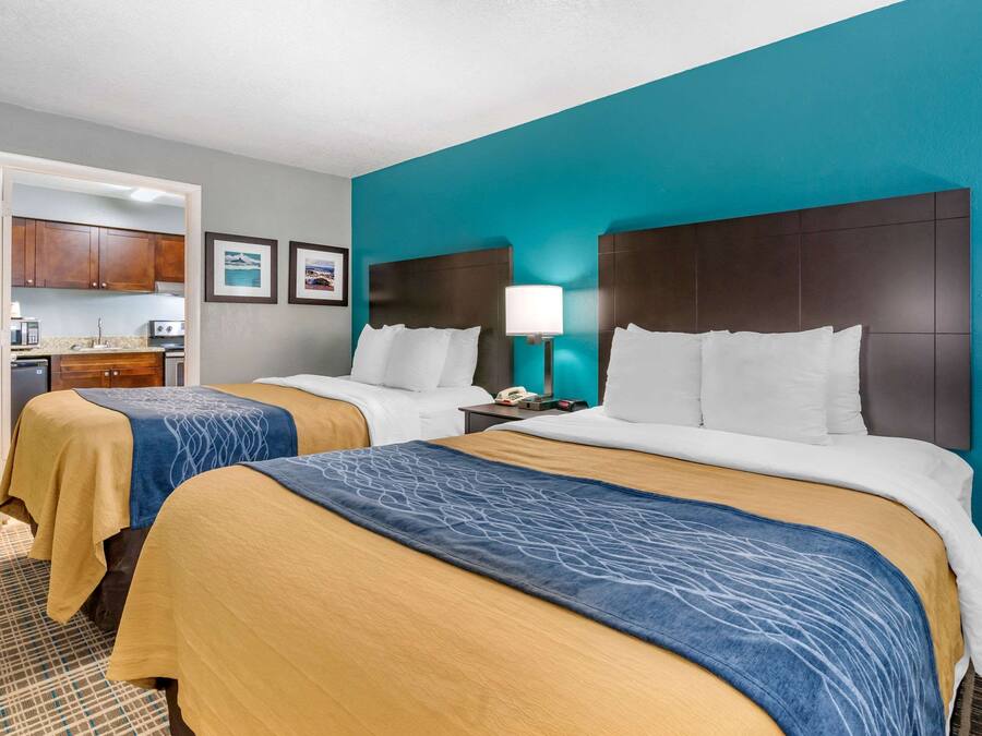 Quarto de hotel com duas camas, uma cozinha compacta e um banheiro.