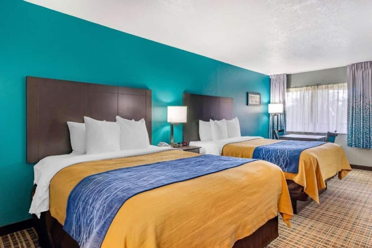 Habitación de hotel con dos camas, paredes color aguamarina y una ventana con cortinas.