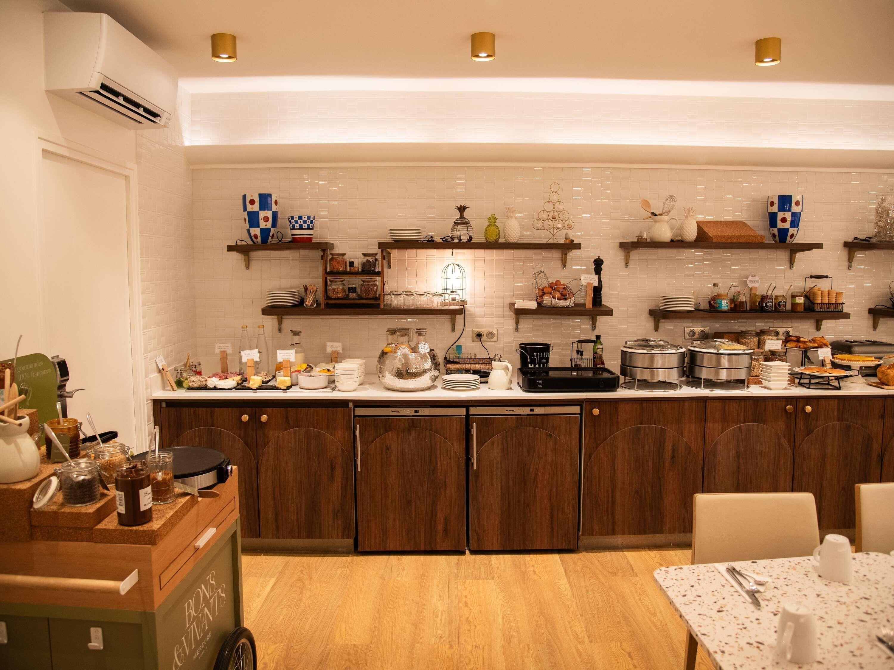 A modern kitchen with wooden cabinets, a breakfast bar, and various food items displayed on shelves.