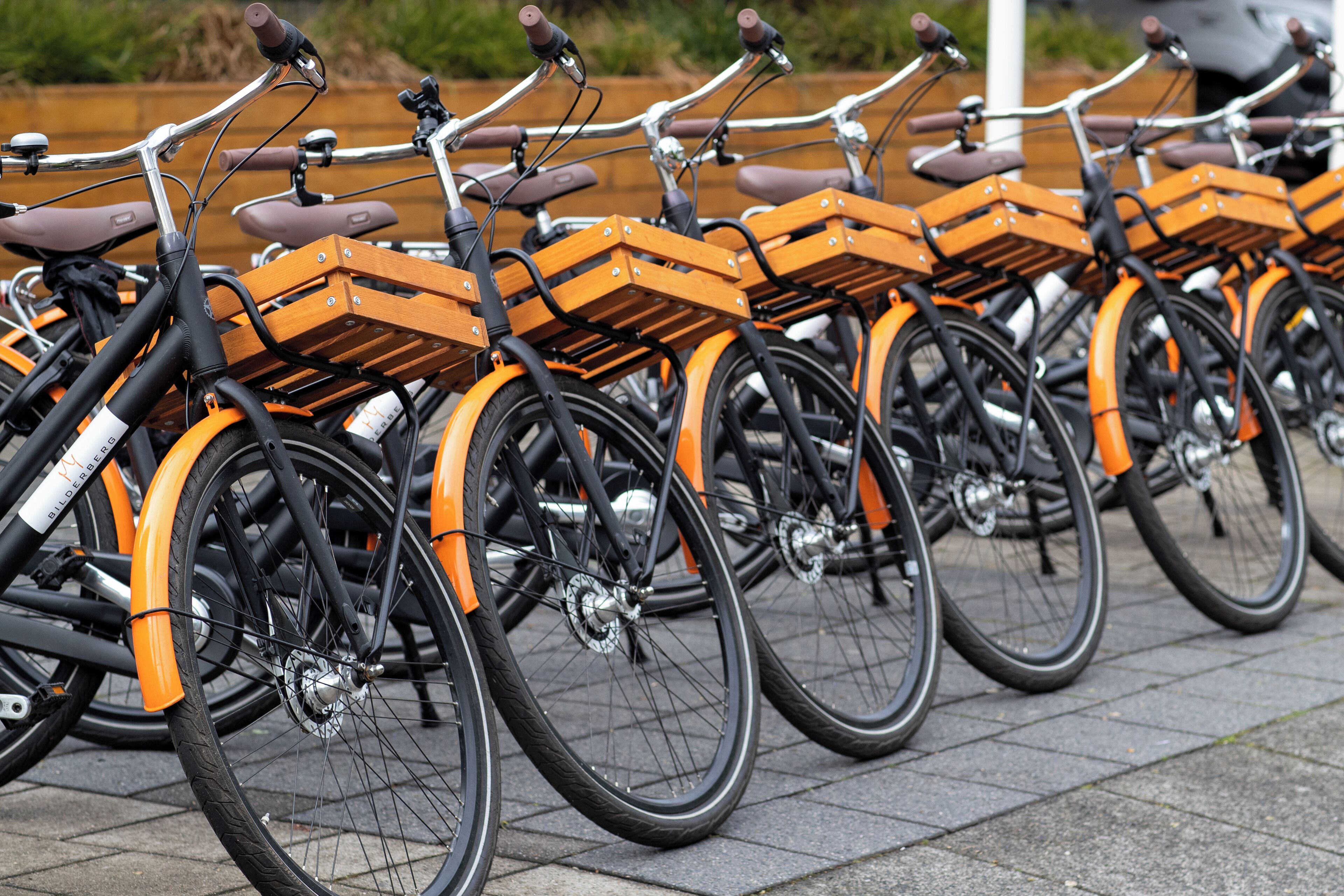 Eine Reihe Fahrräder mit orangefarbenen Rahmen und Holzkorben, auf einem befestigten Untergrund abgestellt.
