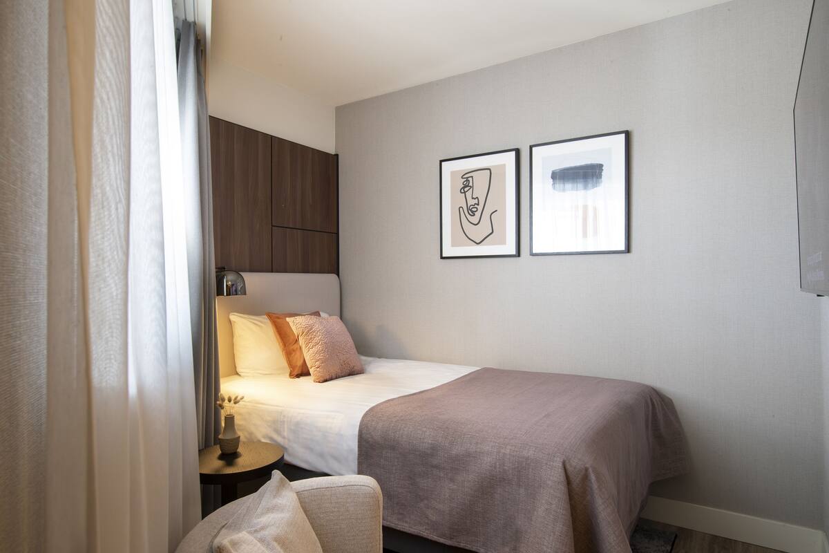 Een slaapkamer met een bed, een nachtkastje, een stoel en twee ingelijste kunstwerken aan de muur.