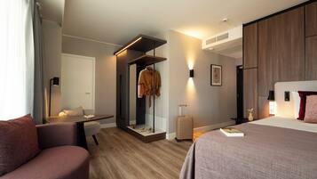 Una habitación de hotel moderna con piso de madera, una cama con almohada roja, un escritorio con silla, un armario y una maleta.