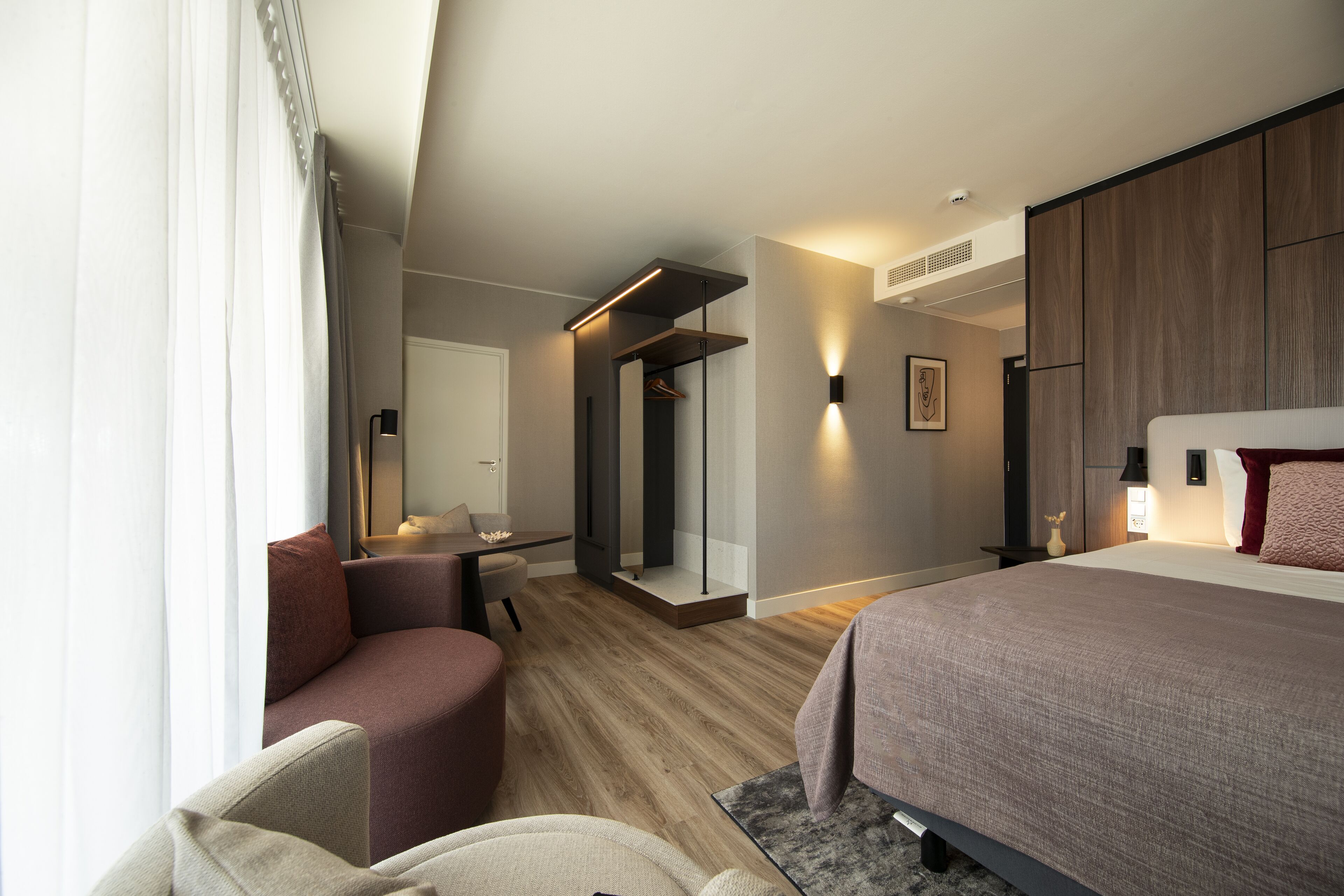 Een moderne hotelkamer met een bed, zithoek en een inloopkast.