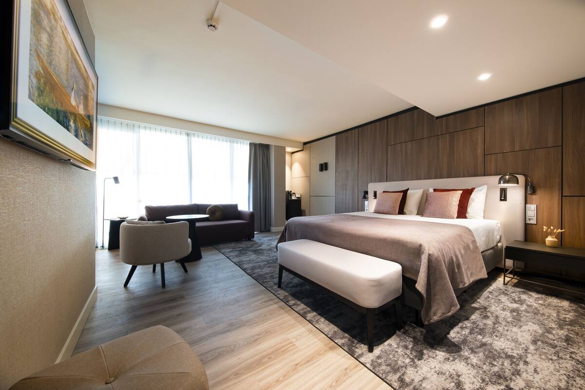 Een moderne slaapkamer met een groot bed, een bank, een houten bankje en een bureau.