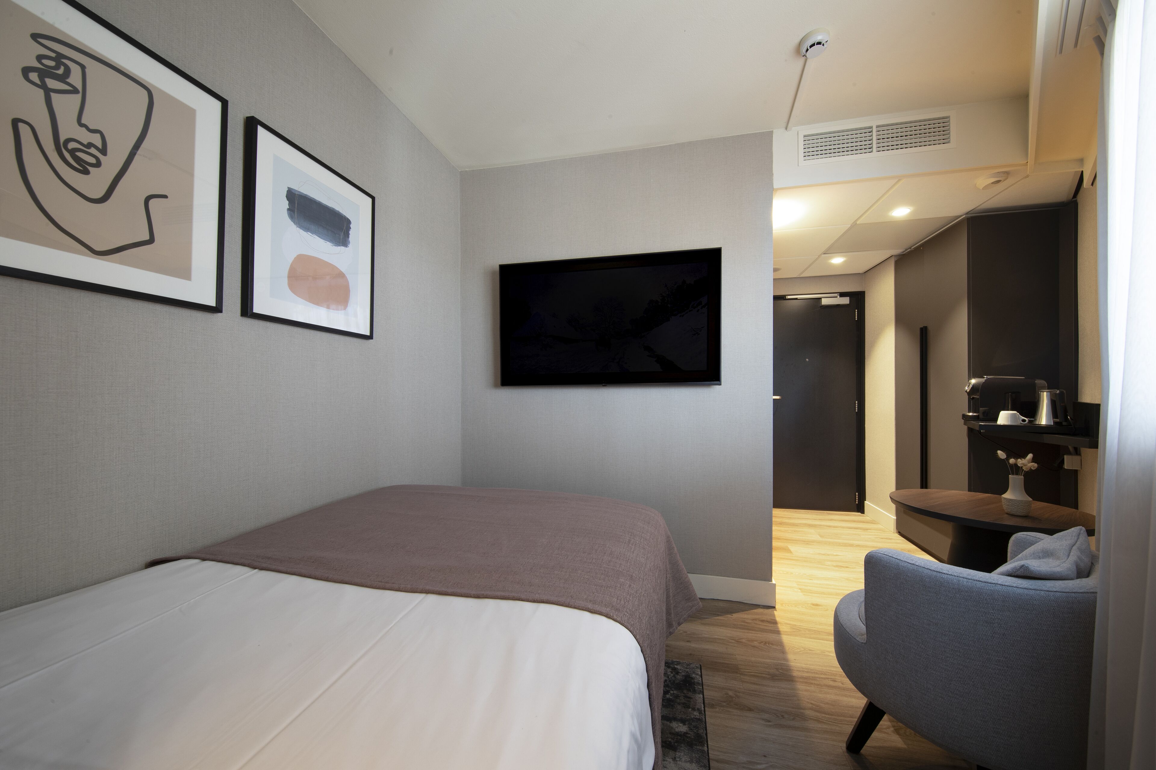 A modern hotel room with a bed, a flat-screen TV, and a seating area with a chair and table.