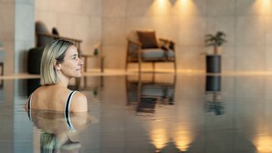 Una persona en una piscina interior moderna con vista despejada al borde, una silla de descanso y una mesita con una planta.
