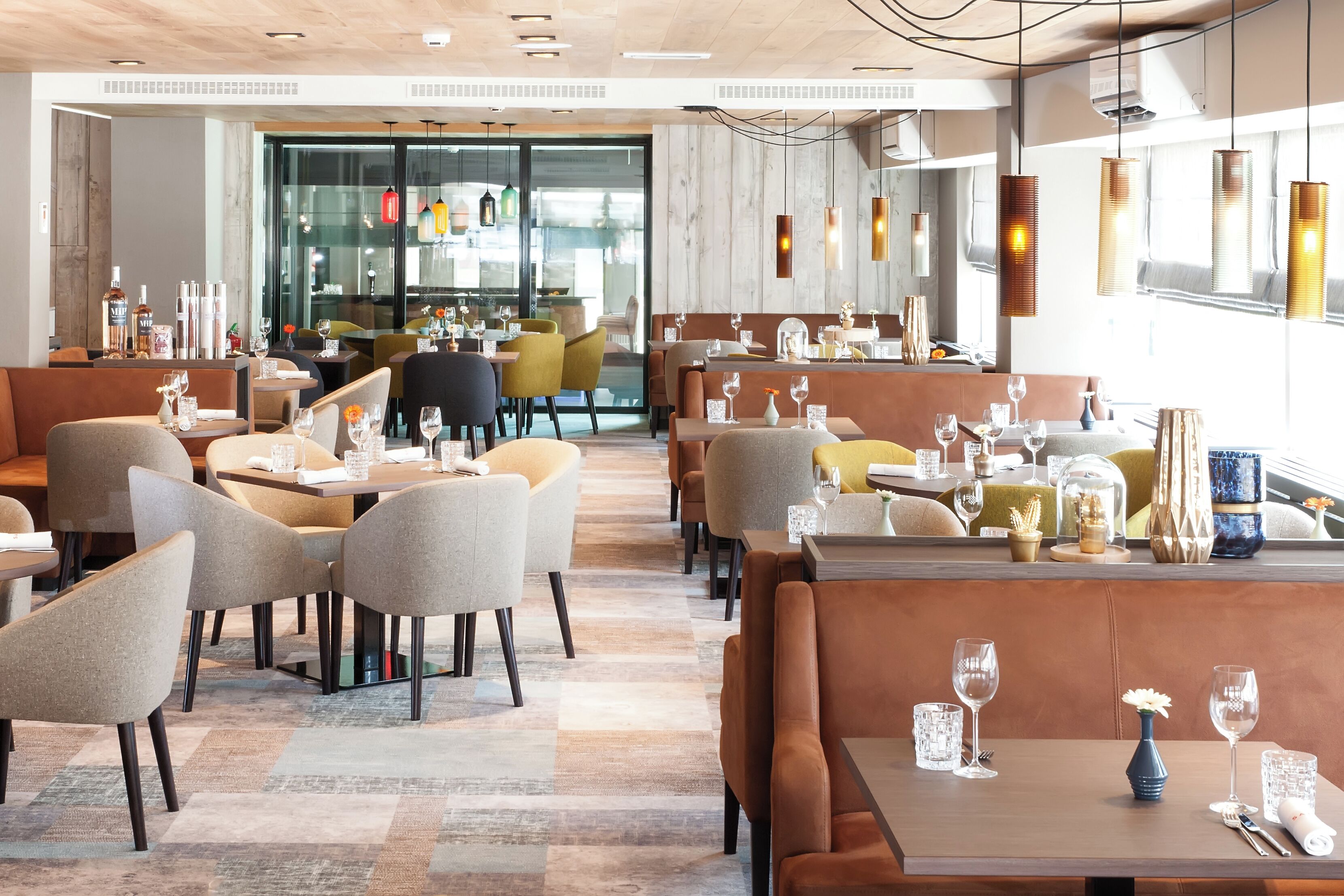 A modern restaurant with booths and tables, wooden flooring, and pendant lighting.