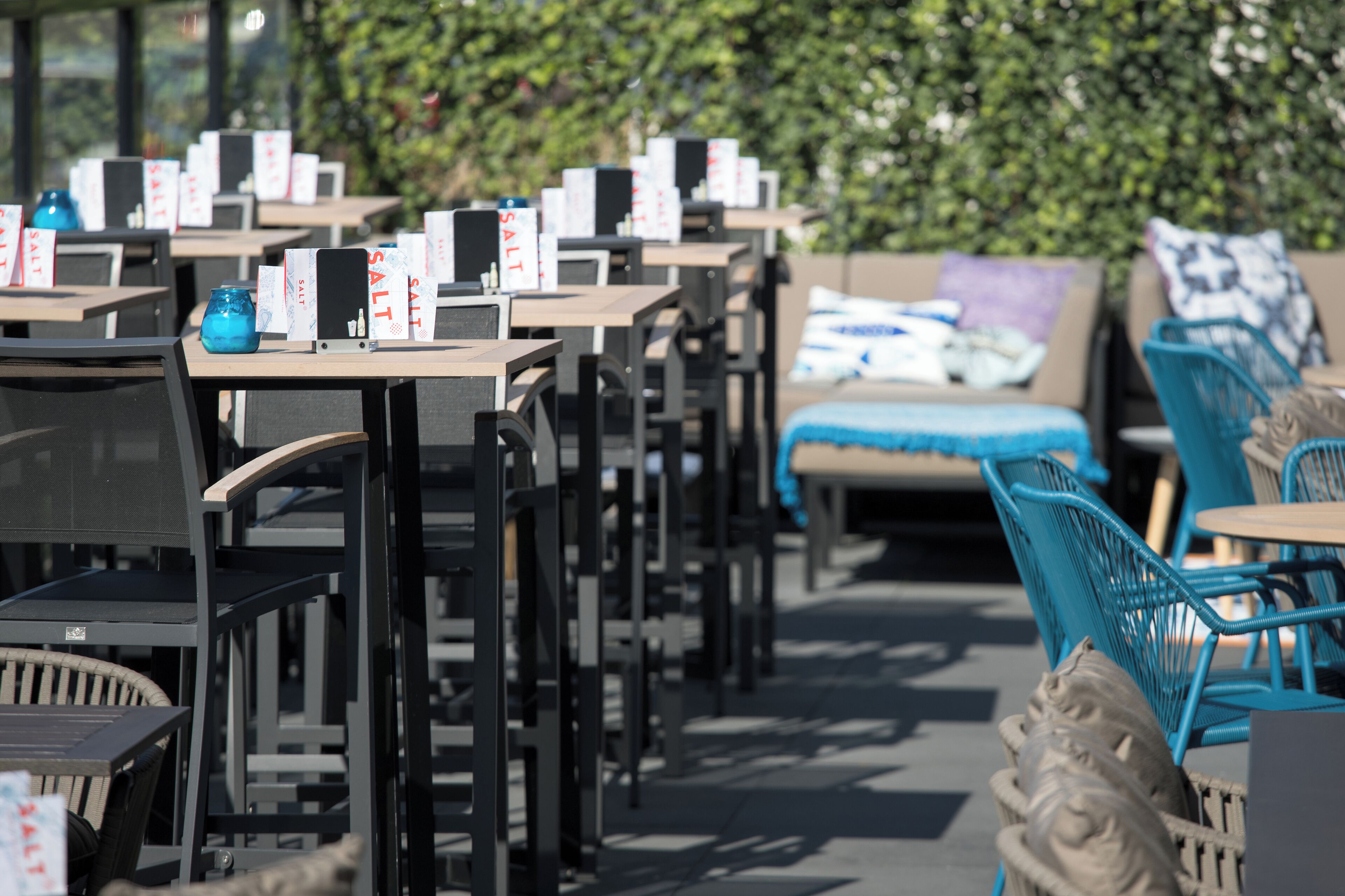 Outdoor dining tables with chairs, some with blue cushions, and signs indicating salt.