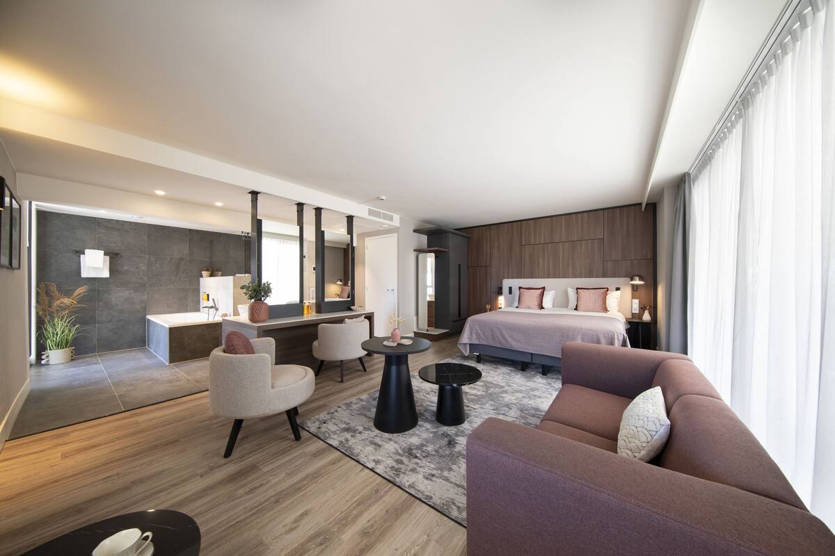Een moderne hotelkamer met een groot bed, een zithoek met een bank en stoelen, een klein tafeltje en een grote spiegel.