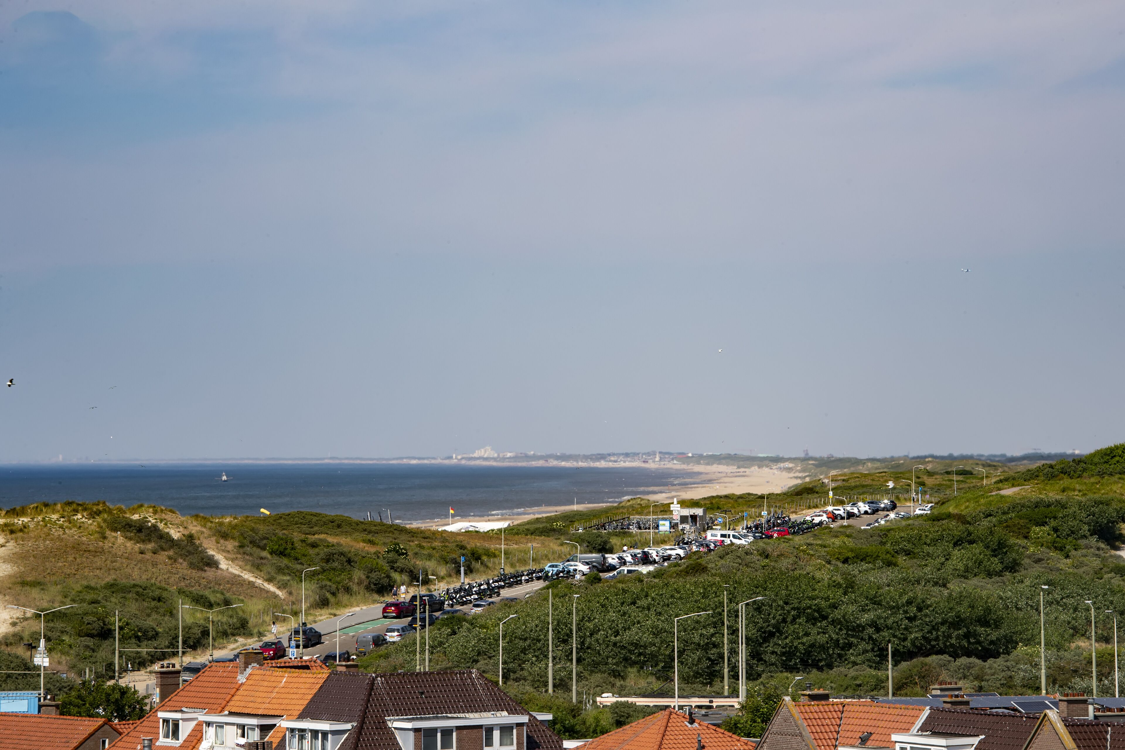 A coastal road with parked cars, leading to a beach.