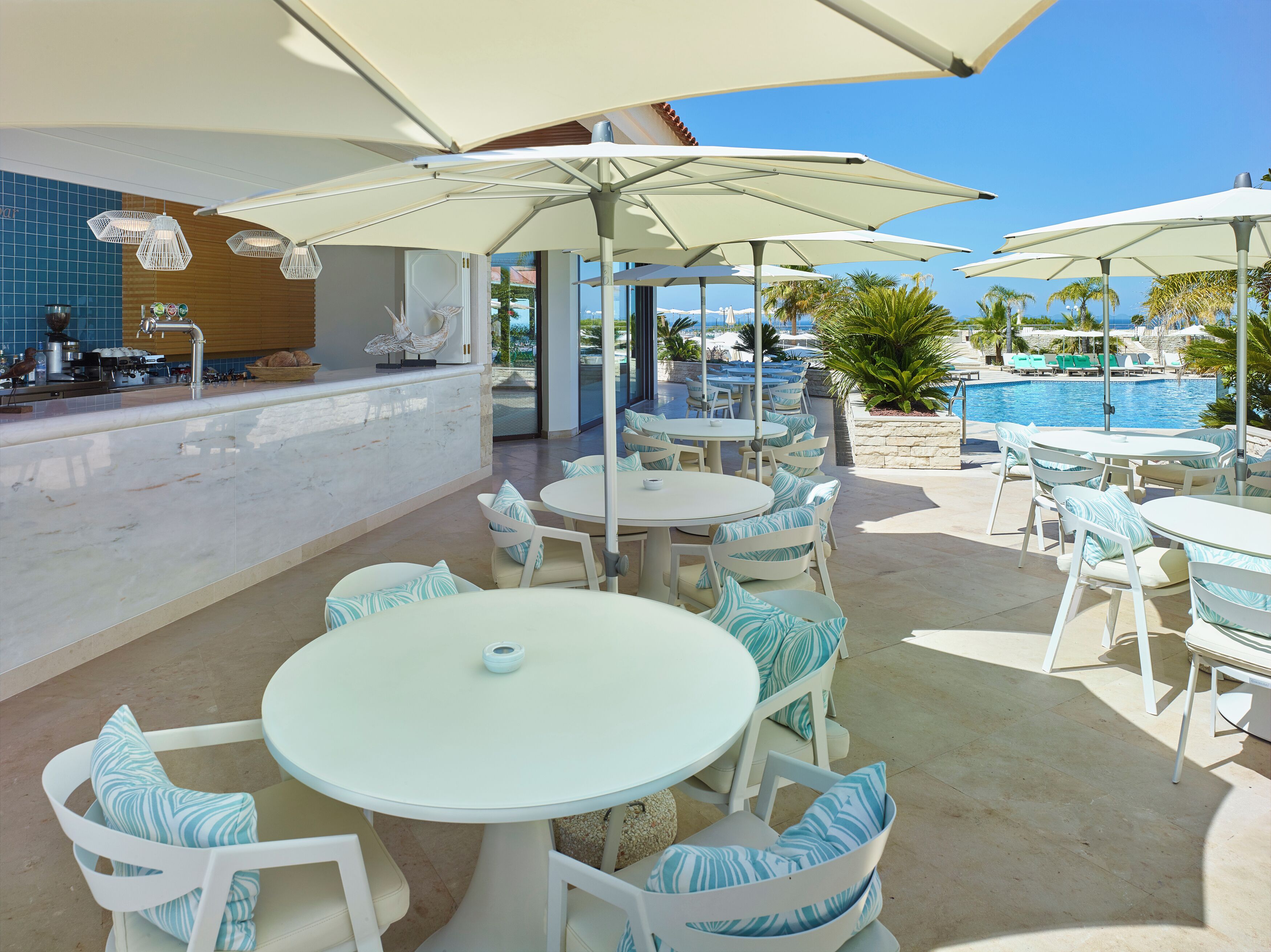 Zona junto a la piscina con mobiliario exterior y sombrillas, un bar y vistas a la piscina y al océano.