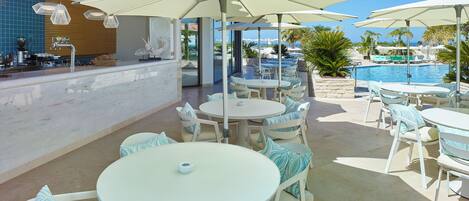 Zona junto a la piscina con mobiliario exterior y sombrillas, un bar y vistas a la piscina y al océano.
