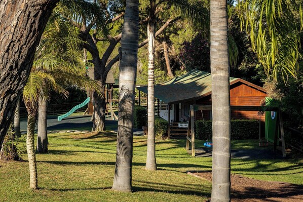 Um parque com um parquinho, uma estrutura de madeira e um edifício com telhado verde.