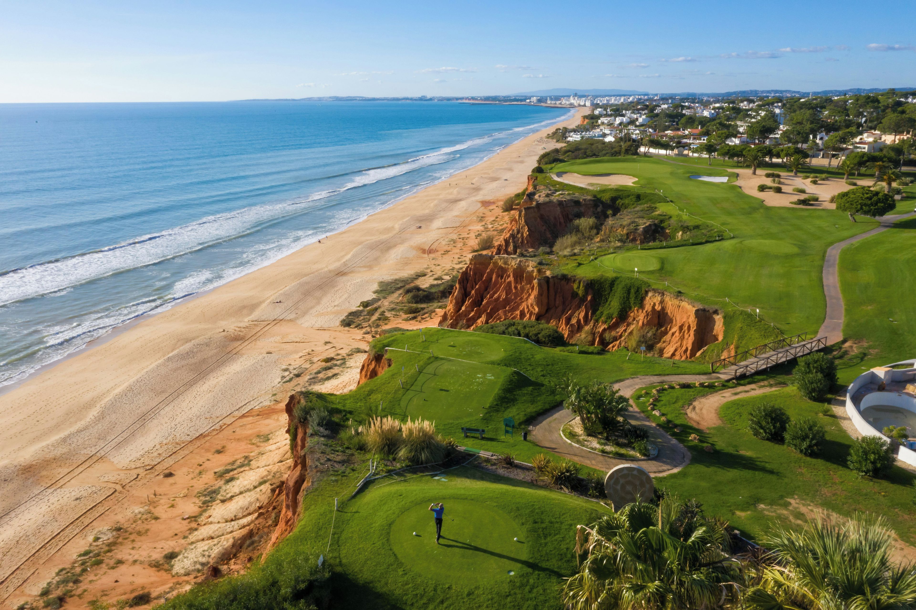 Un campo de golf frente al mar, con playa, casas y cielo despejado.