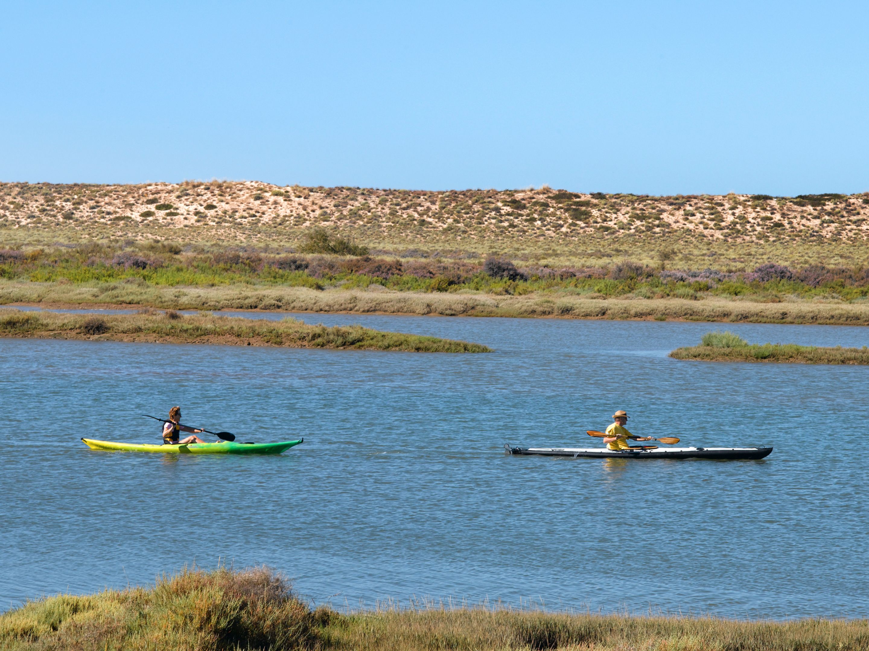 Dos kayaks sobre un cuerpo de agua tranquilo, con un paisaje montañoso al fondo.