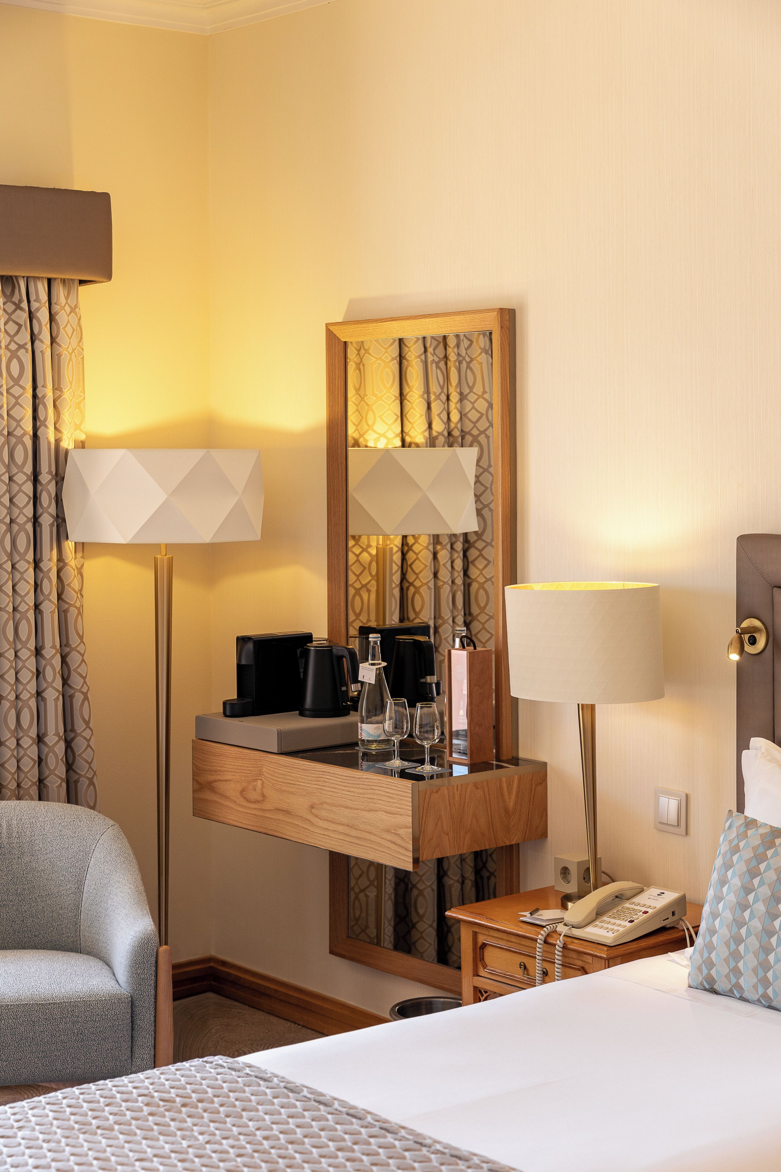 A hotel room with a bed, a desk with a coffee maker, a telephone, and a chair.